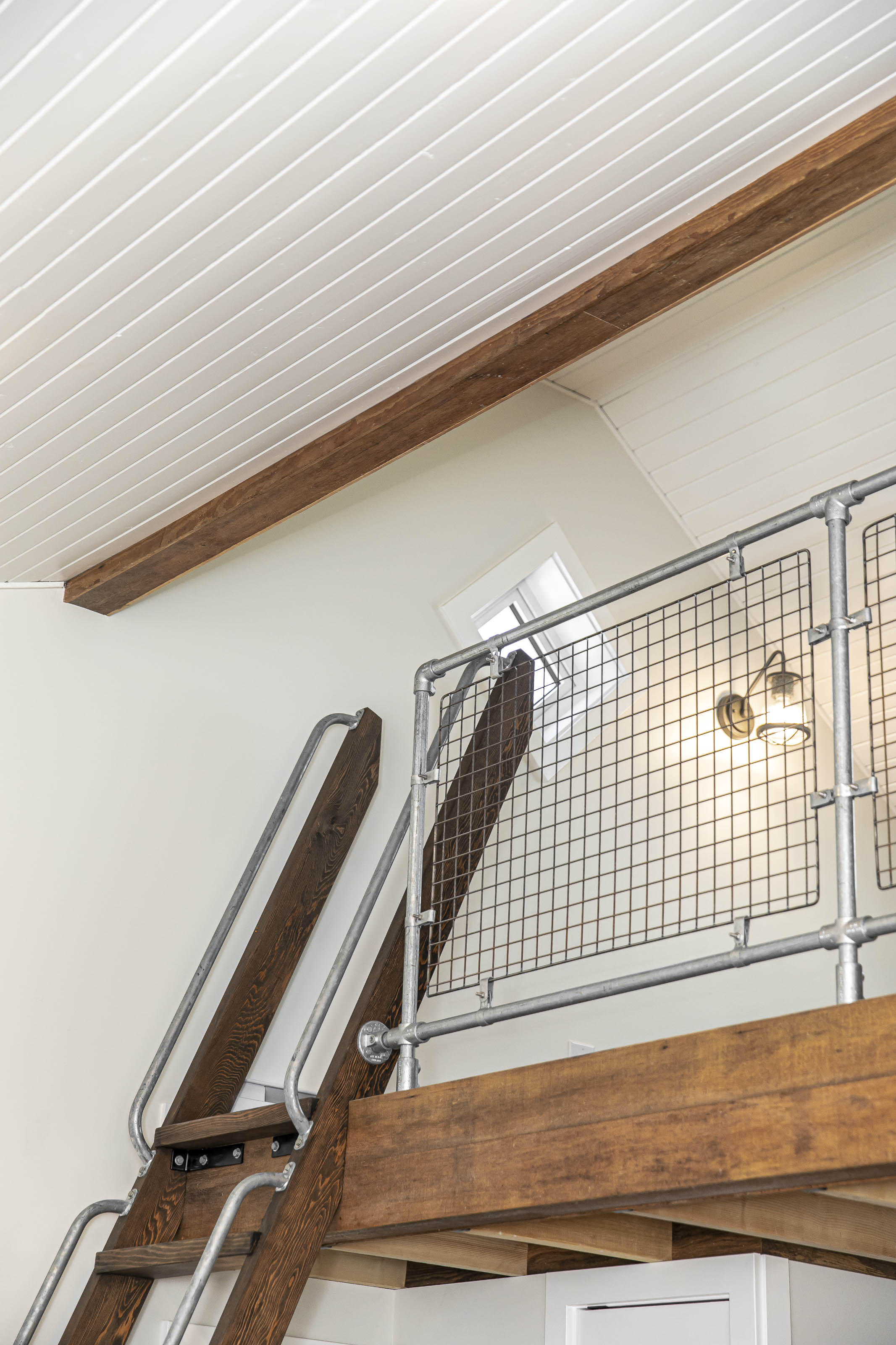 Industrial-style loft ladder with dark-stained wood treads and metal railing leading to an upper mezzanine in a Victoria carriage house
