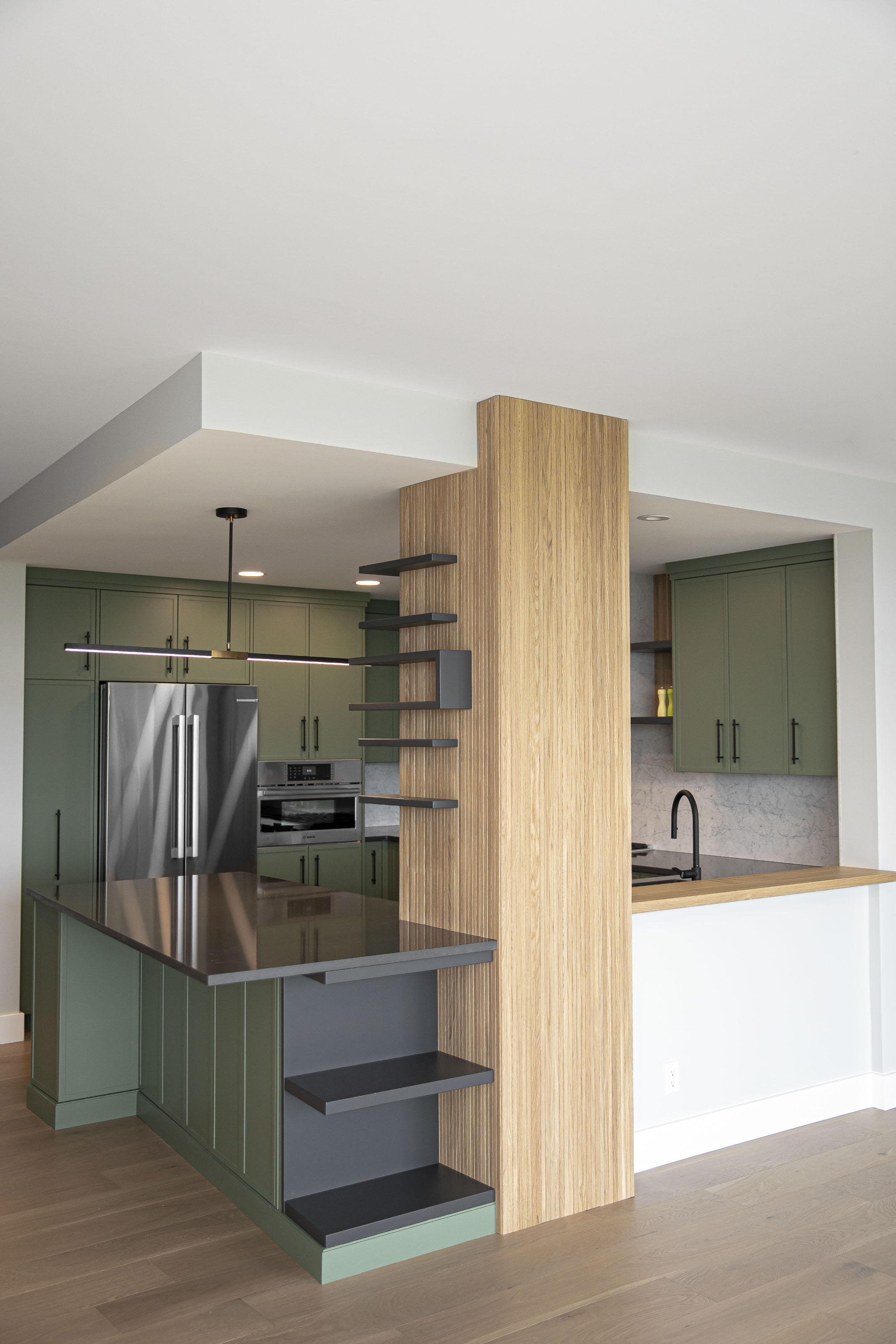 Full kitchen remodel with green cabinetry, black quartz island, and open tambour shelving, completed by Outlook Project Management in Victoria, British Columbia