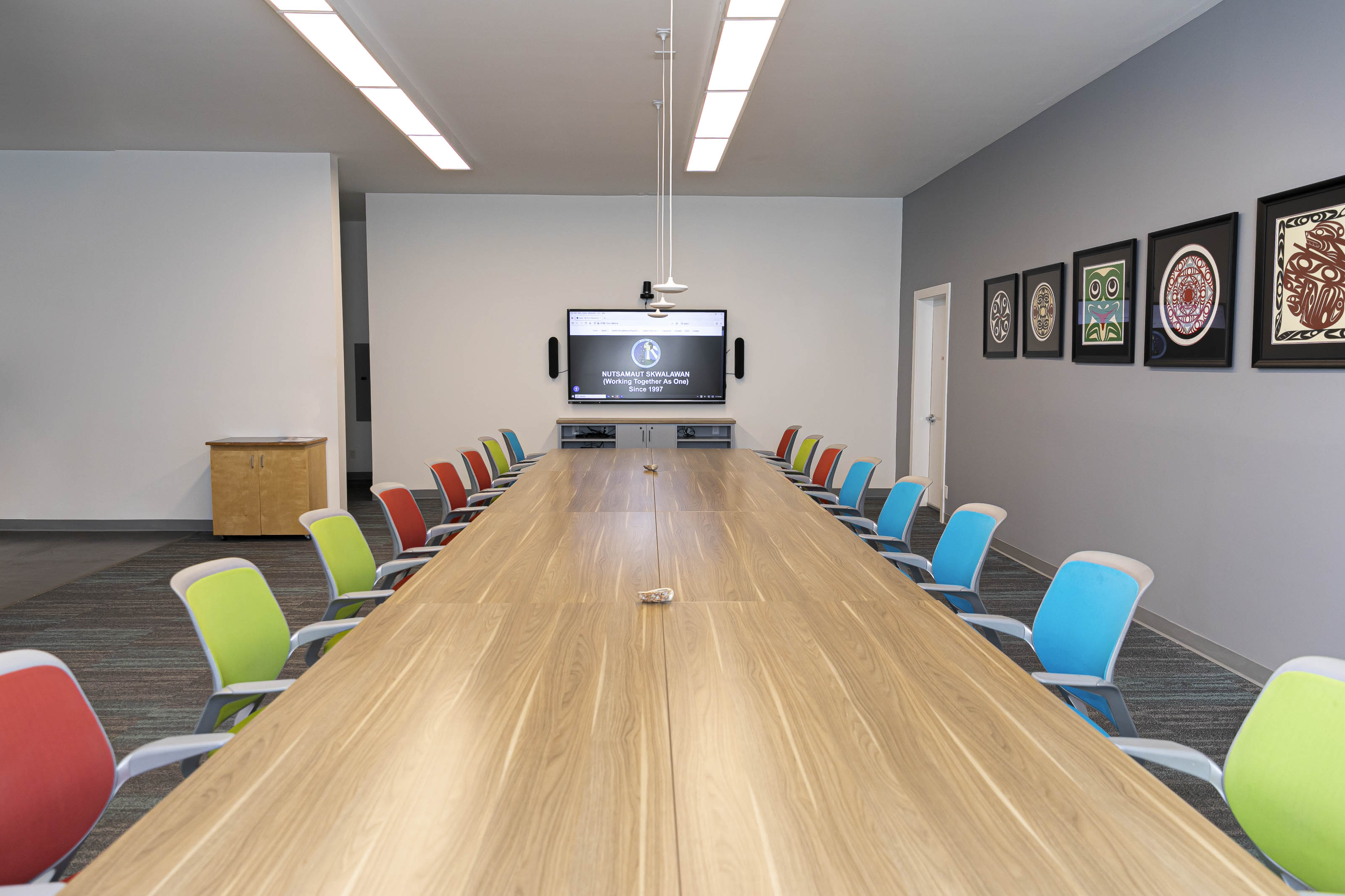 Modern conference room renovation by Outlook Project Management Victoria BC - cultural family center featuring long wooden table, colorful ergonomic chairs, Indigenous artwork gallery, and integrated AV technology