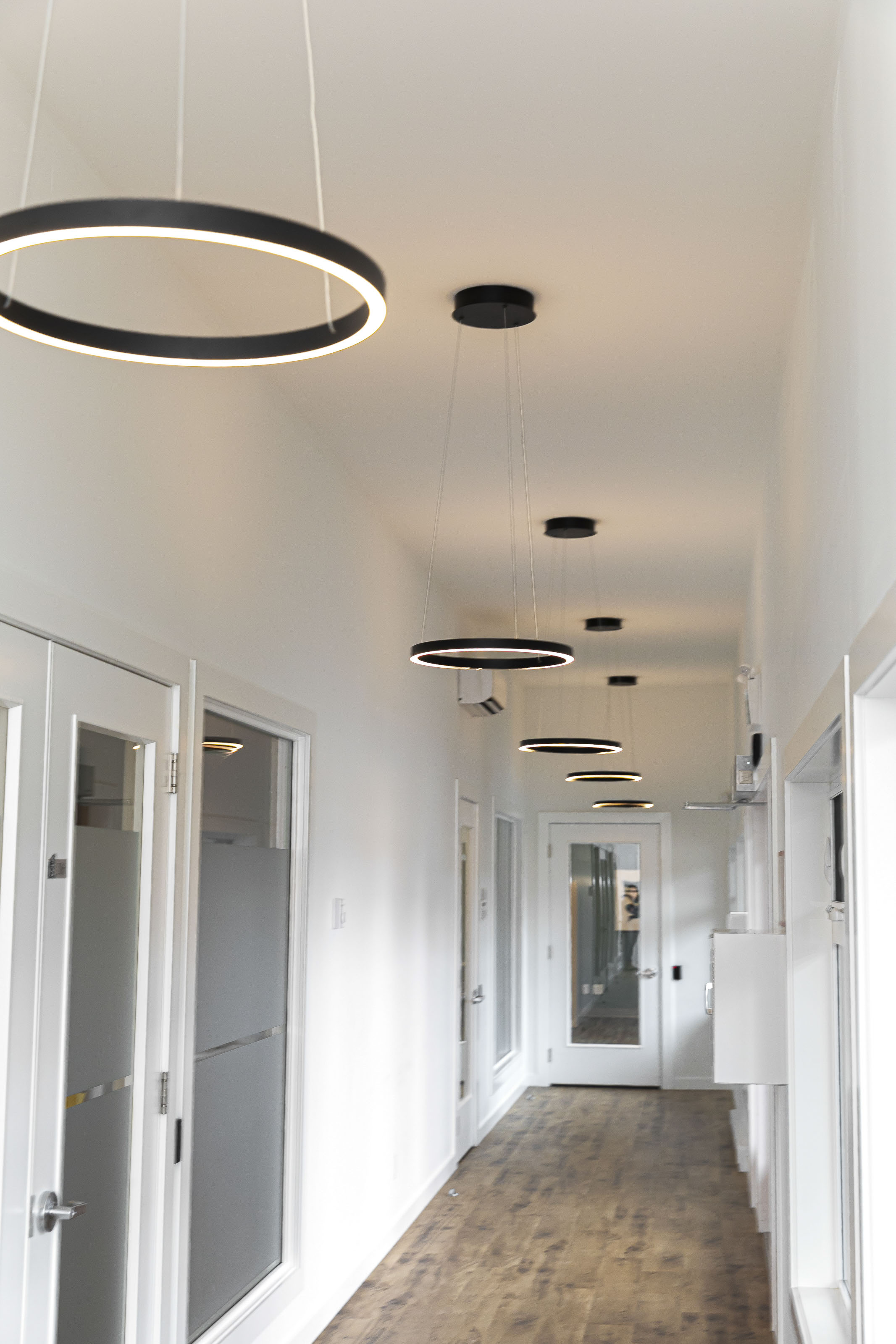 Contemporary hallway design with circular pendant lighting Victoria BC - cultural family center renovation by Outlook Project Management featuring modern fixtures and glass office partitions