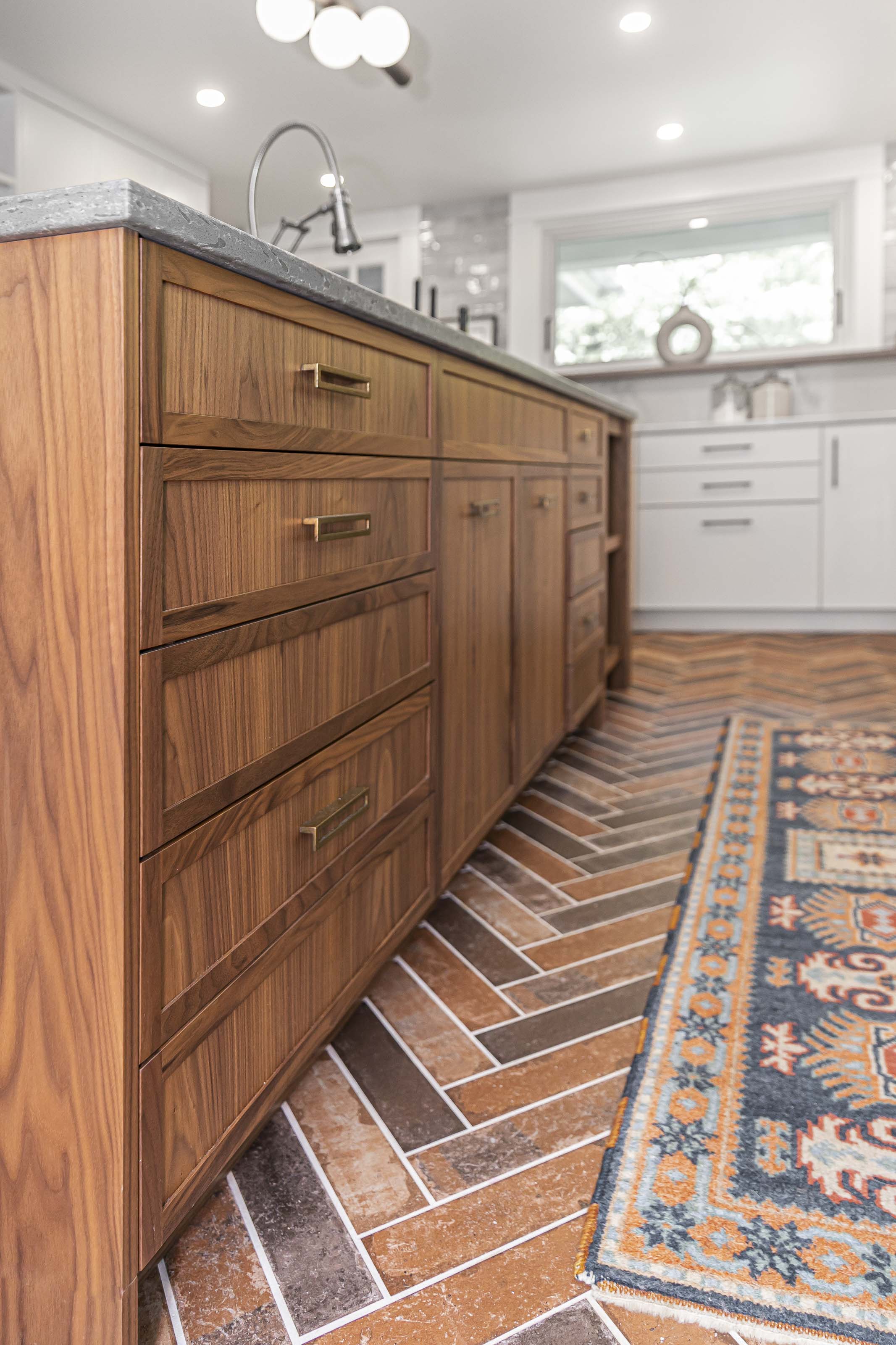 Custom walnut kitchen island with matte black stone countertops and brick-patterned tile flooring, completed by Outlook Project Management in Victoria BC.