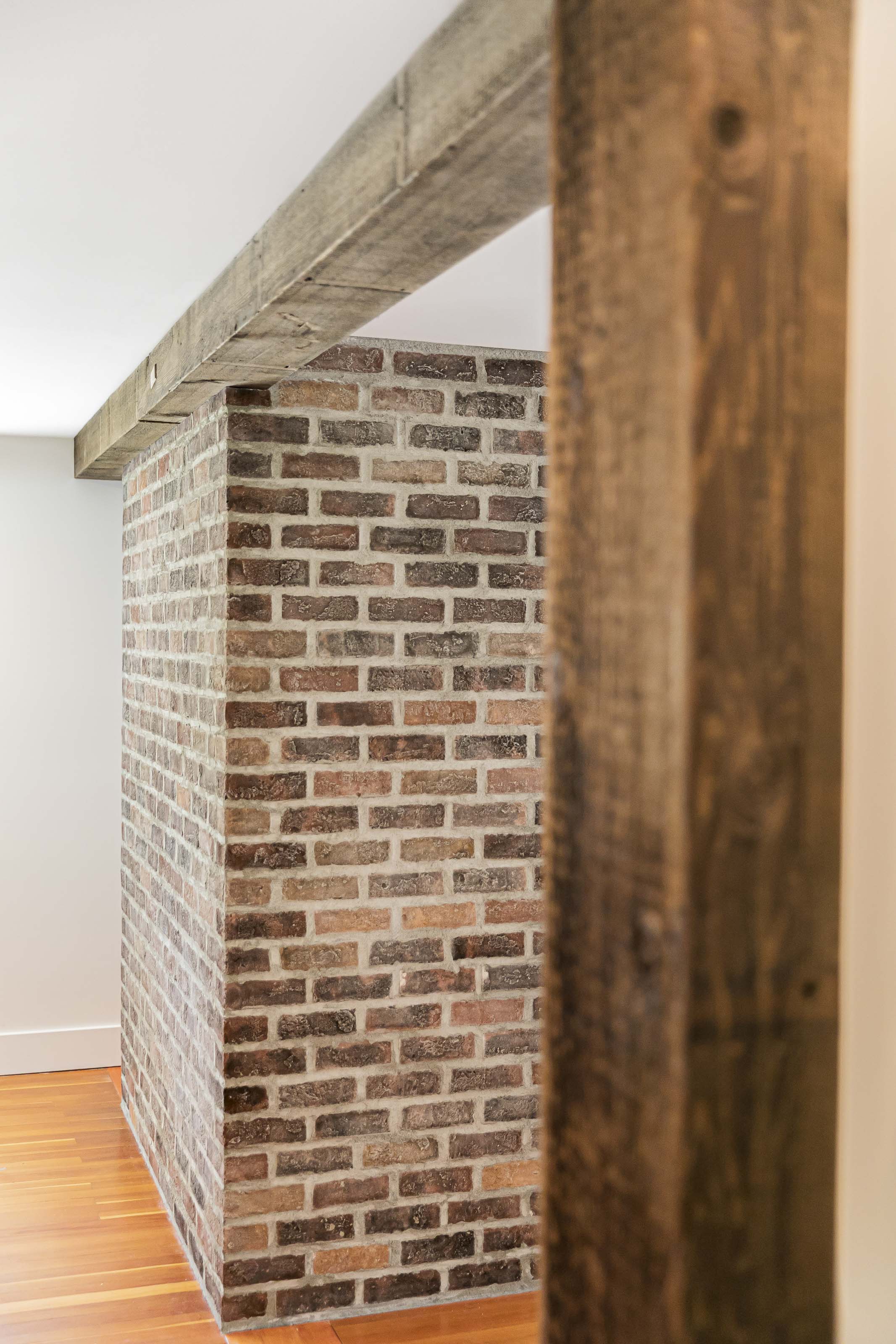 Reclaimed wood ceiling beams and exposed brick feature wall in a renovated Victoria home by Outlook Project Management.
