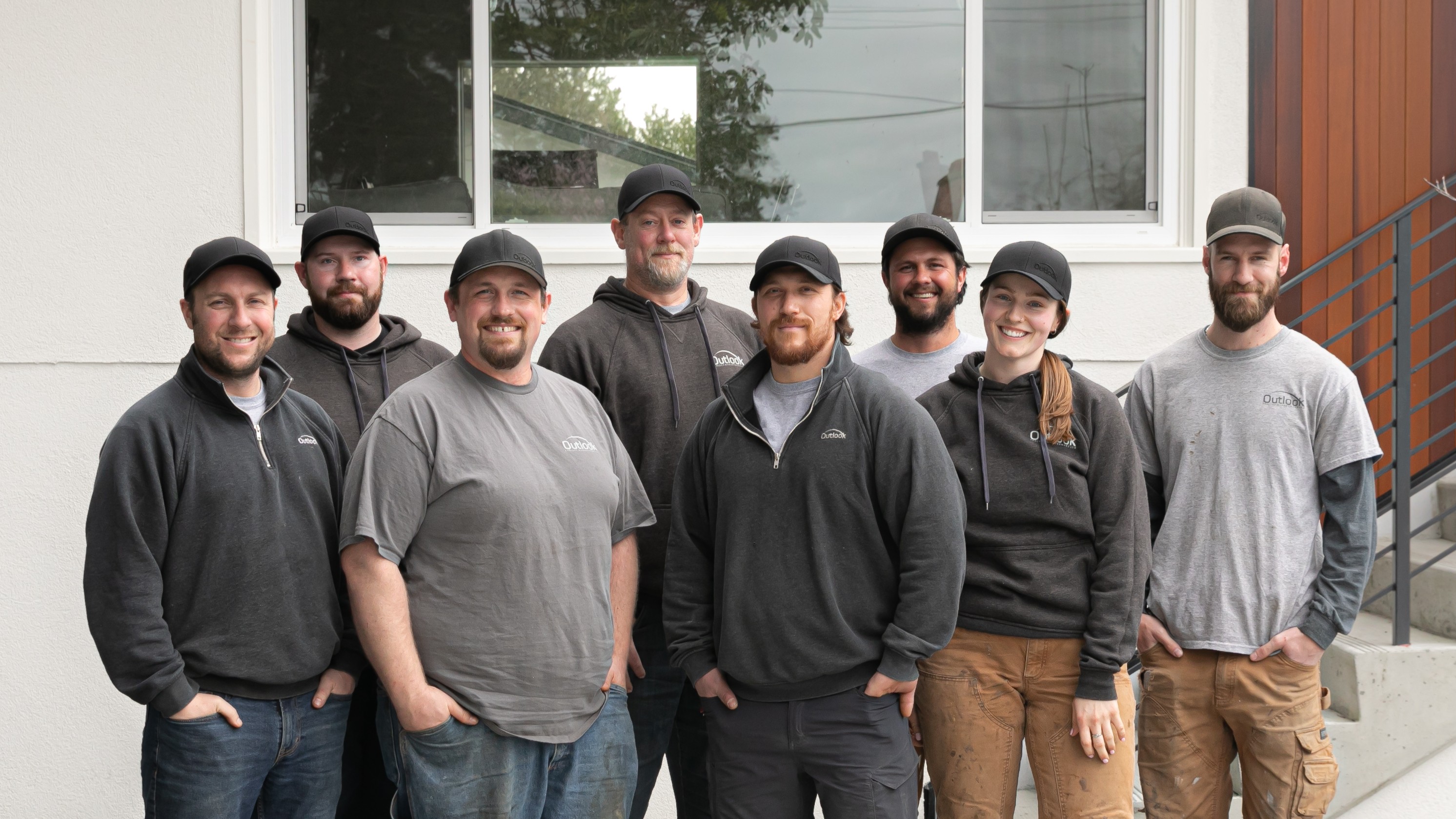 Outlook Project Management crew standing outside a completed residential project, representing the diverse and skilled team featured on the Our Team profile page. The image reflects the company's approachable, hands-on culture and commitment to craftsmanship in Victoria, BC.