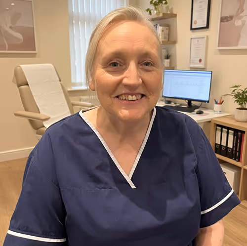 Smiling female healthcare professional wearing navy scrubs in a medical consultation room.