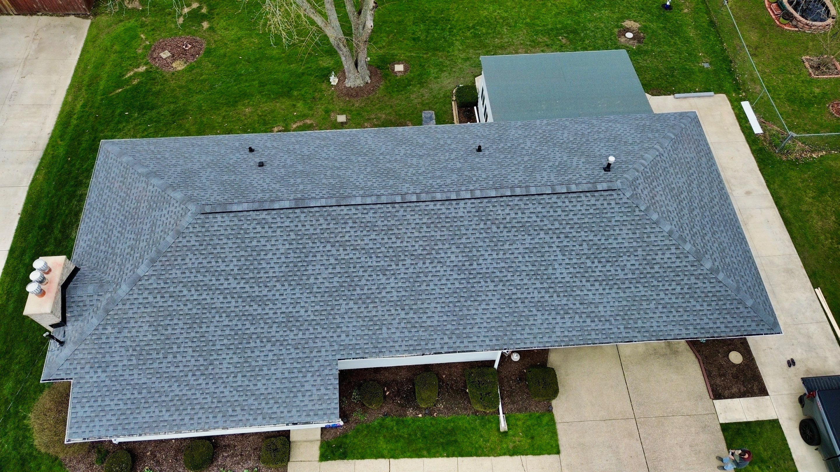 Aerial view of a house roof with gray shingles and surrounding green lawn and walkways.