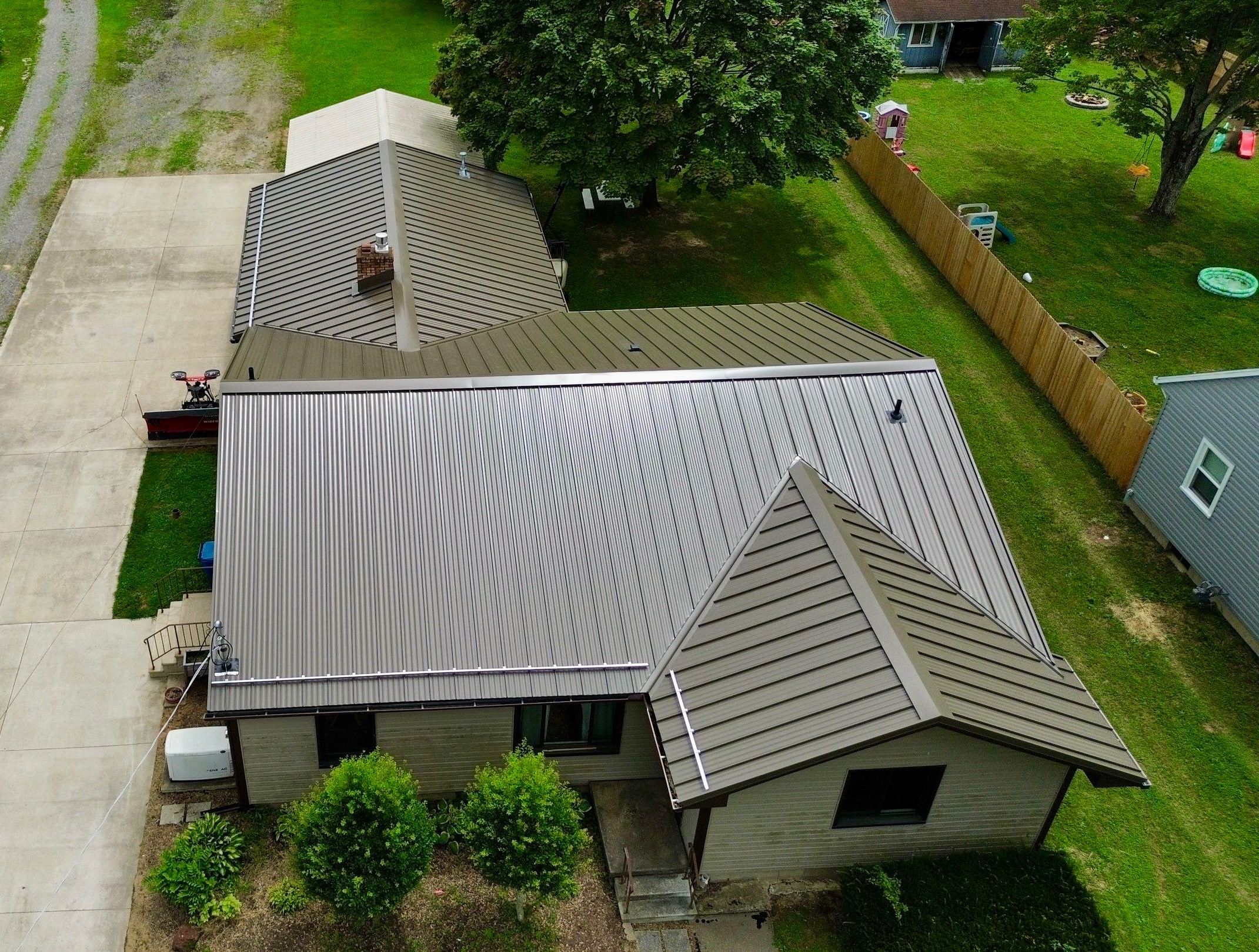 Aerial view of a house with a metal roof, surrounded by grass and nearby structures.
