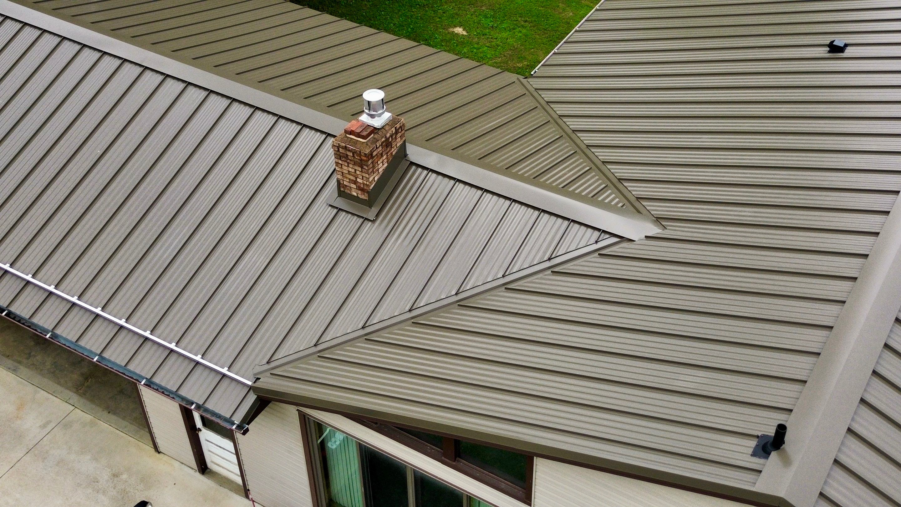 Aerial view of a metal roof with a chimney and adjacent green lawn.