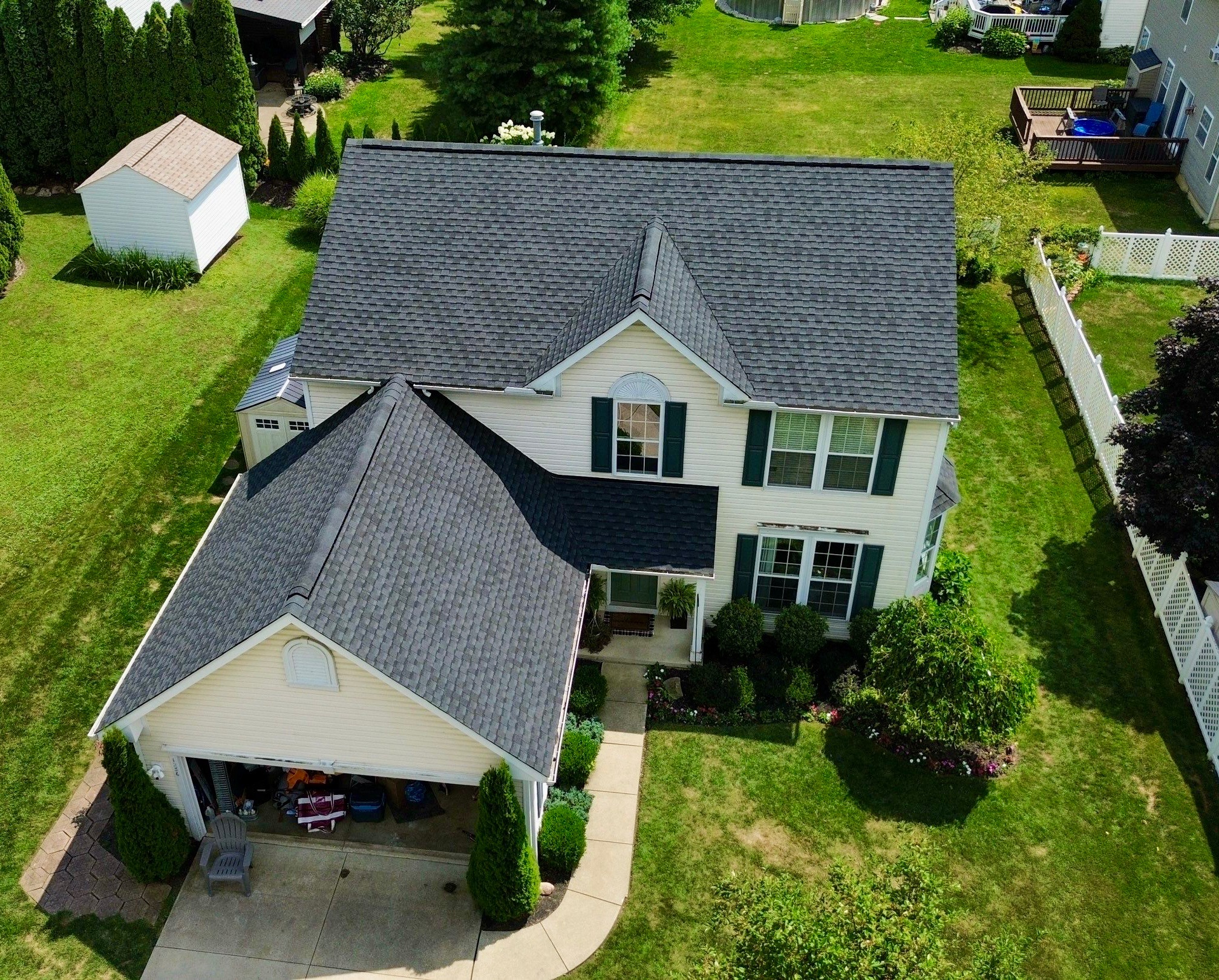 A two-story house with a gabled roof, green shutters, and a neatly landscaped yard is shown from above.