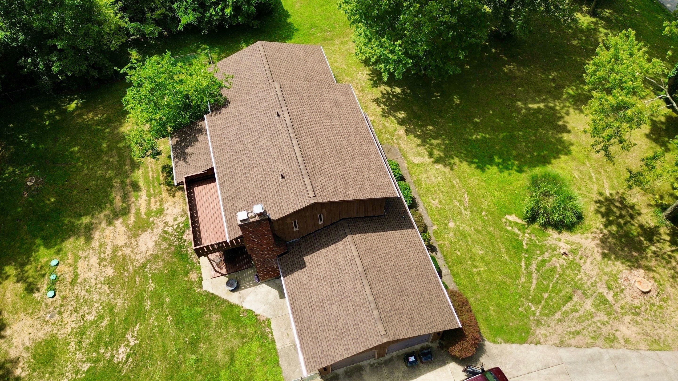 Aerial view of a brown-roofed house surrounded by green grass and trees.