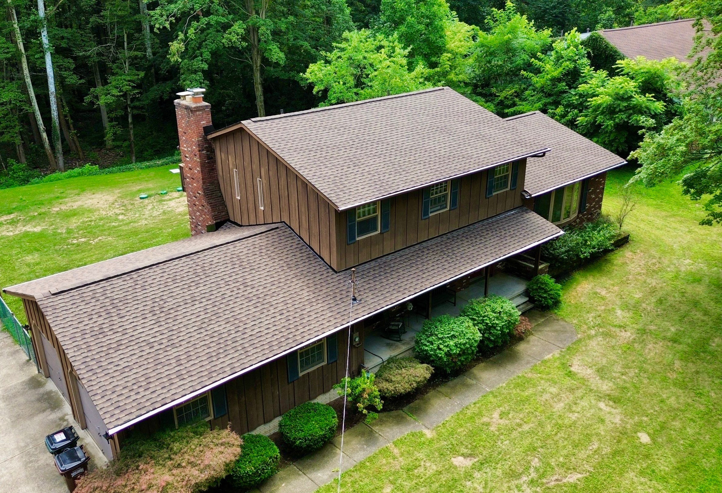 A large, two-story wooden house surrounded by green trees and a grassy yard.