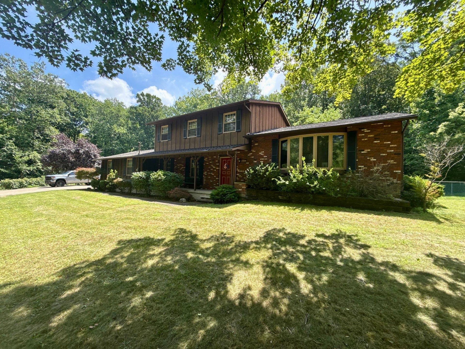 A two-story brick house surrounded by green grass and trees on a sunny day.
