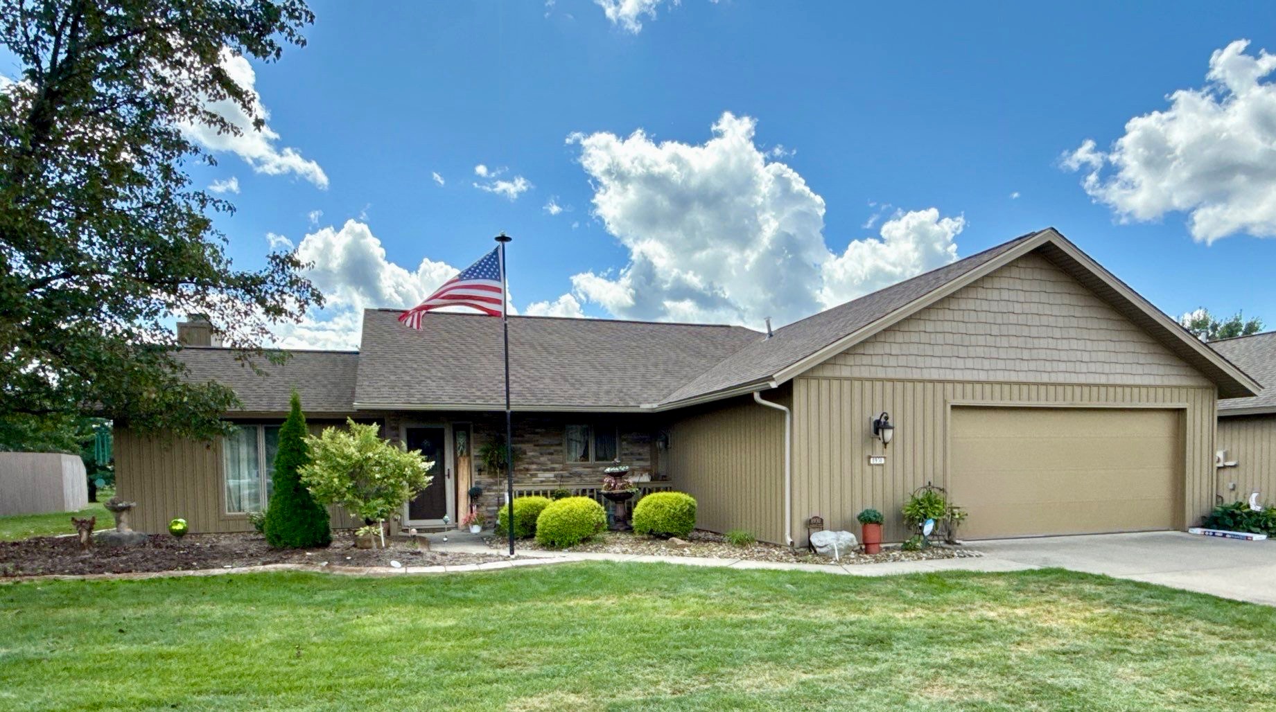 A single-story house with a brown exterior, an American flag, and landscaped front yard features.
