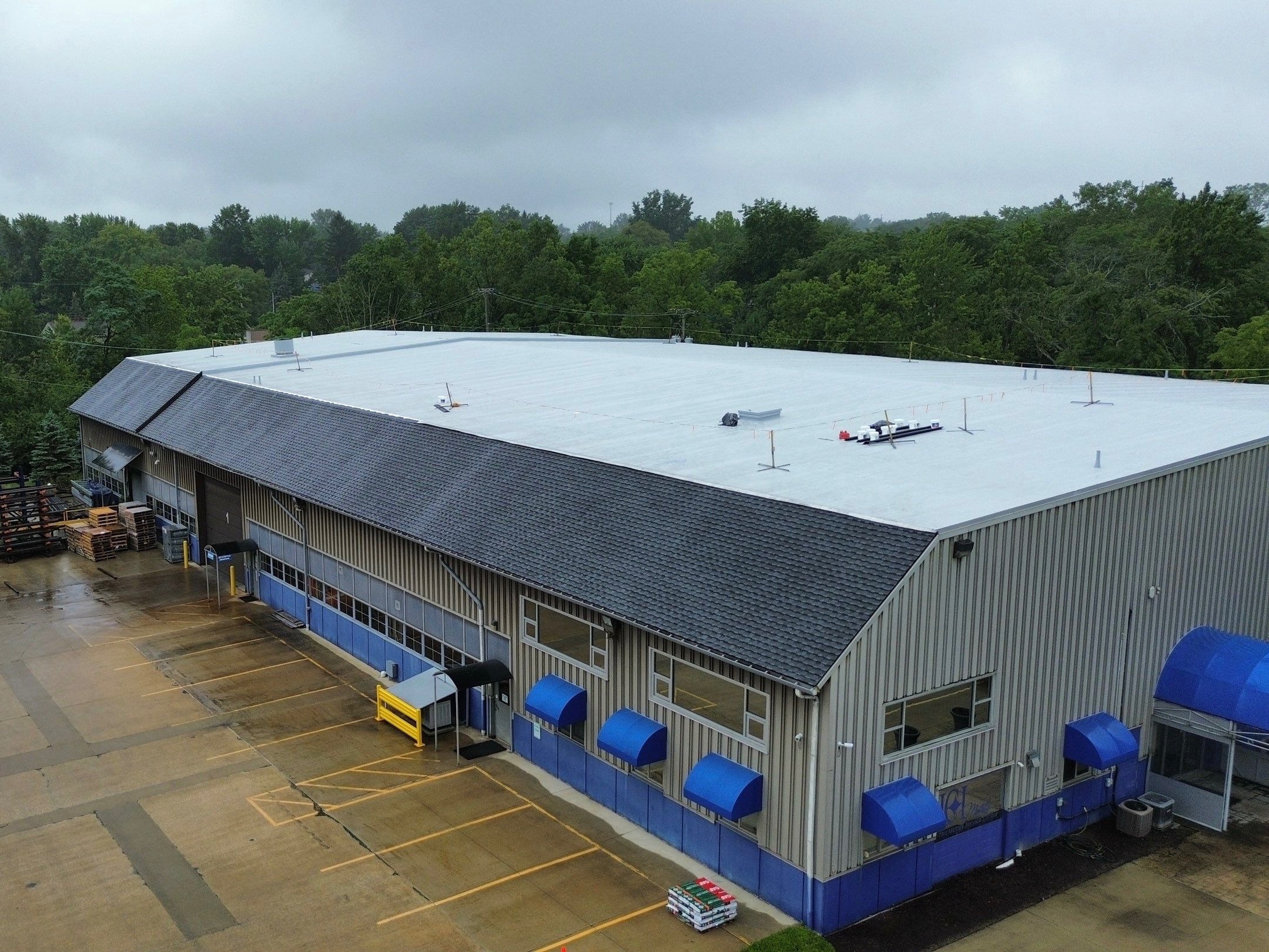 A large commercial building with a gray roof and blue awnings, surrounded by green trees.