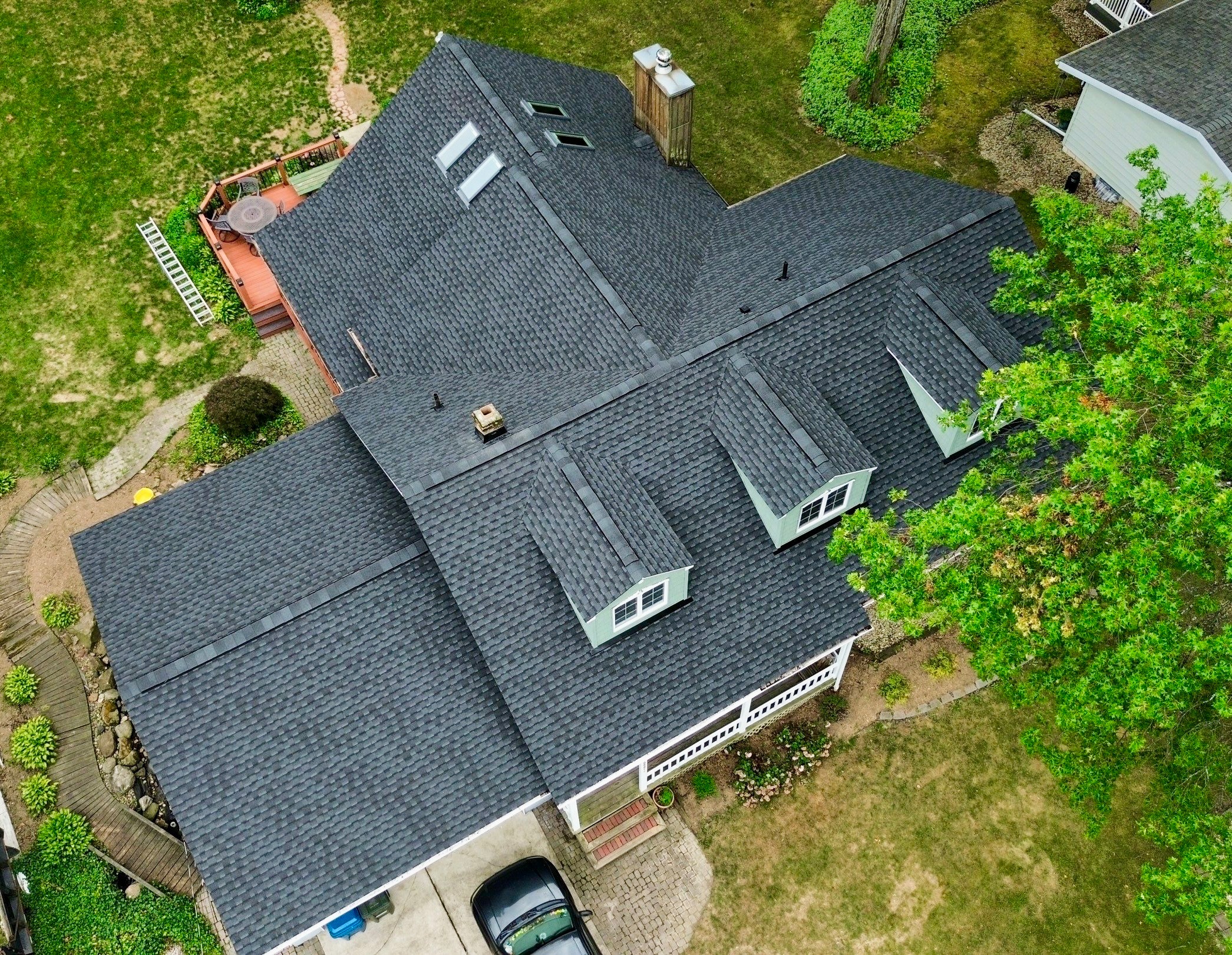 Aerial view of a house with a dark shingle roof and surrounding green lawn and trees.