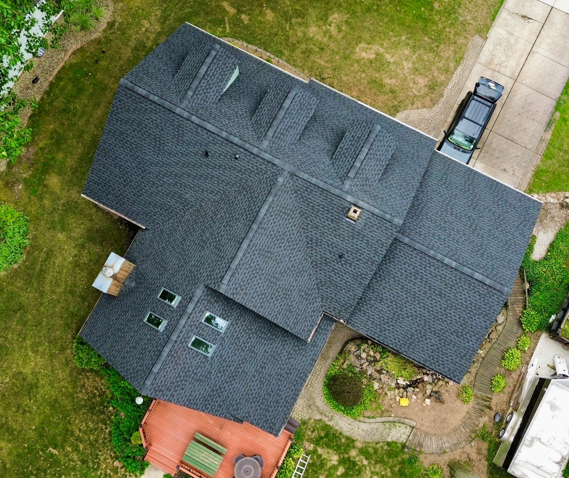Aerial view of a large house with a dark roof and green surrounding landscape.
