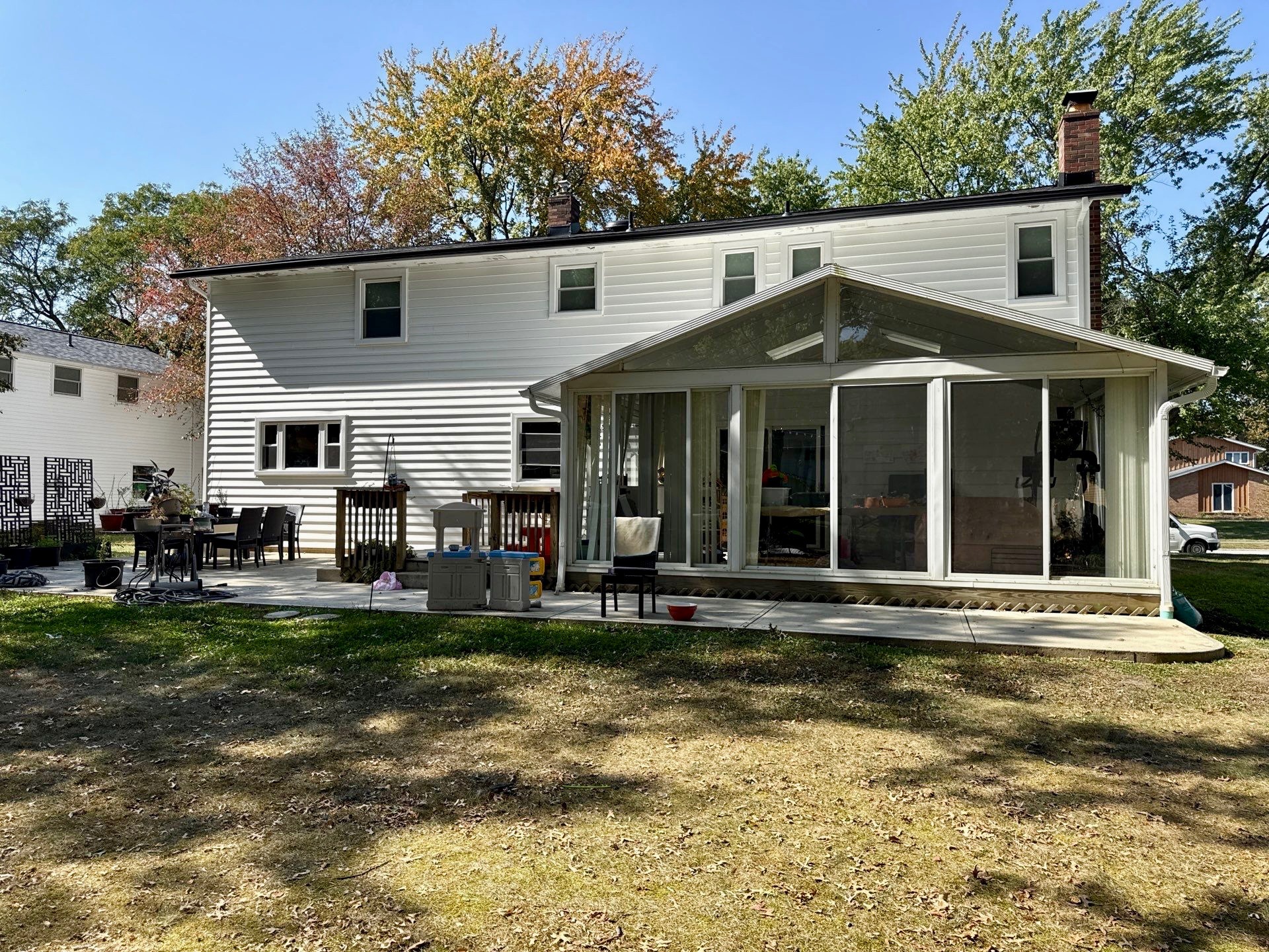 A two-story house with a glass-enclosed porch, surrounded by trees and a grassy yard.
