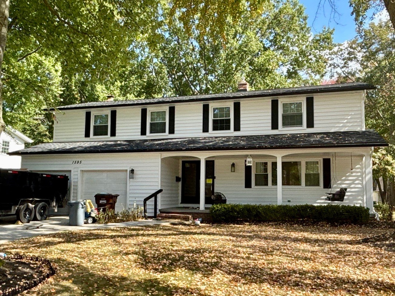 Two-story white house with black shutters, a porch, and scattered autumn leaves in the yard.