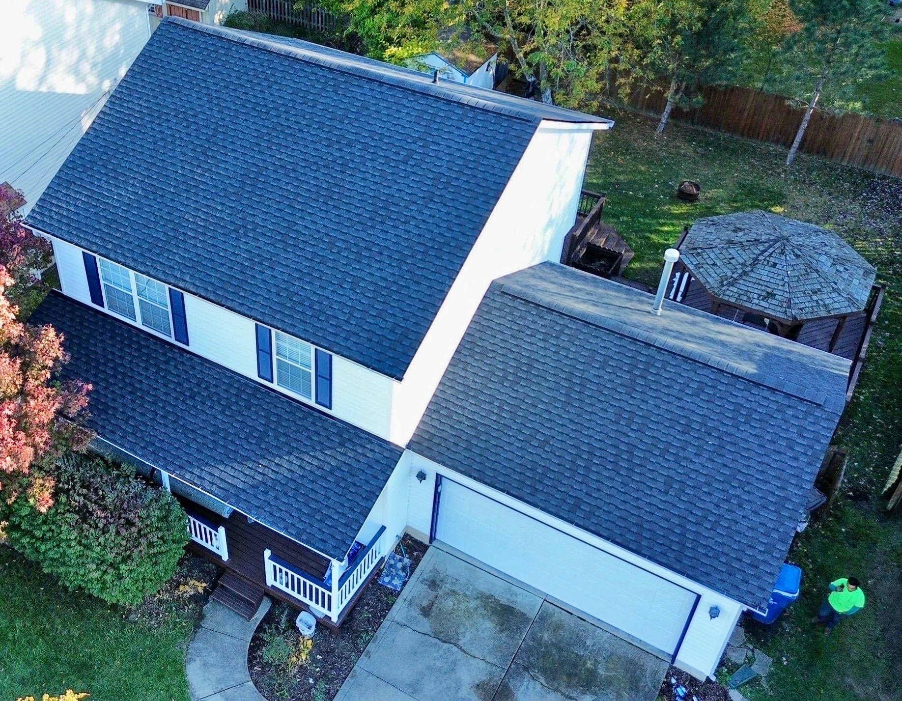 Aerial view of a house featuring a dark shingle roof, white siding, and a gazebo in the backyard.