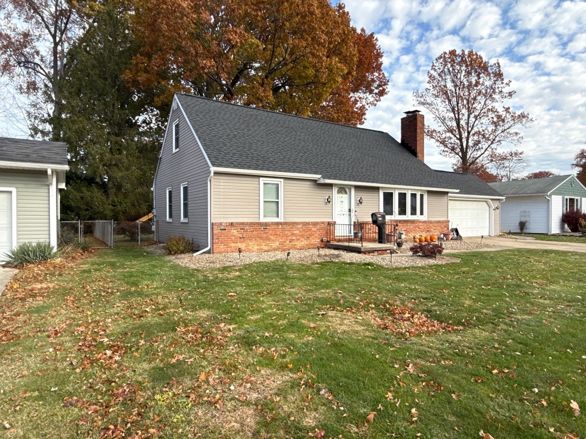 A single-story house with a gray exterior, brick accents, and autumn-colored leaves in the yard.