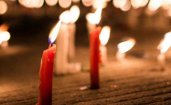 Close-up of lit red candles melting on a textured surface with blurred warm lights in the background.