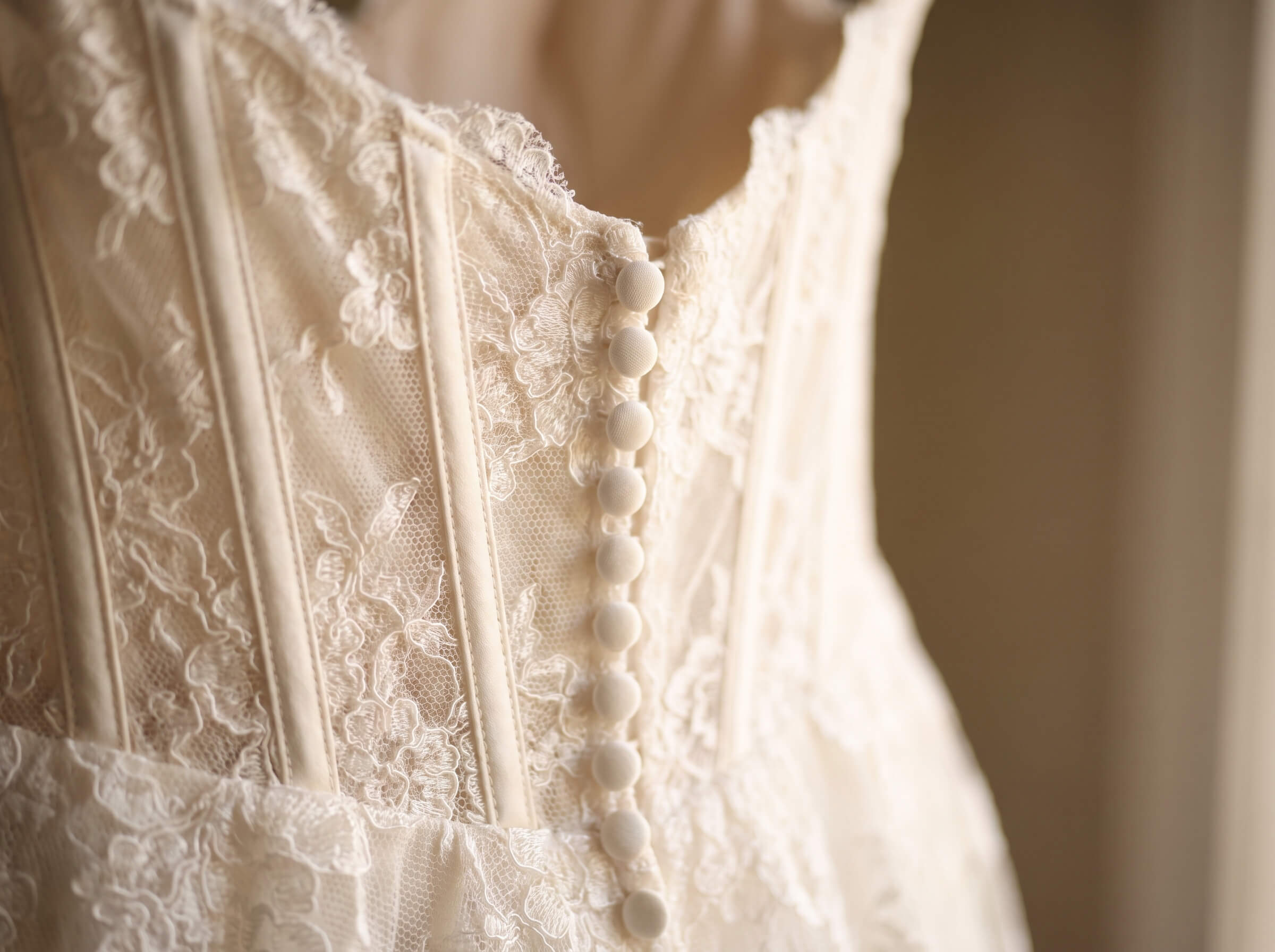 Close-up of the back of an ivory lace wedding dress with a row of fabric-covered buttons and intricate floral lace detailing.