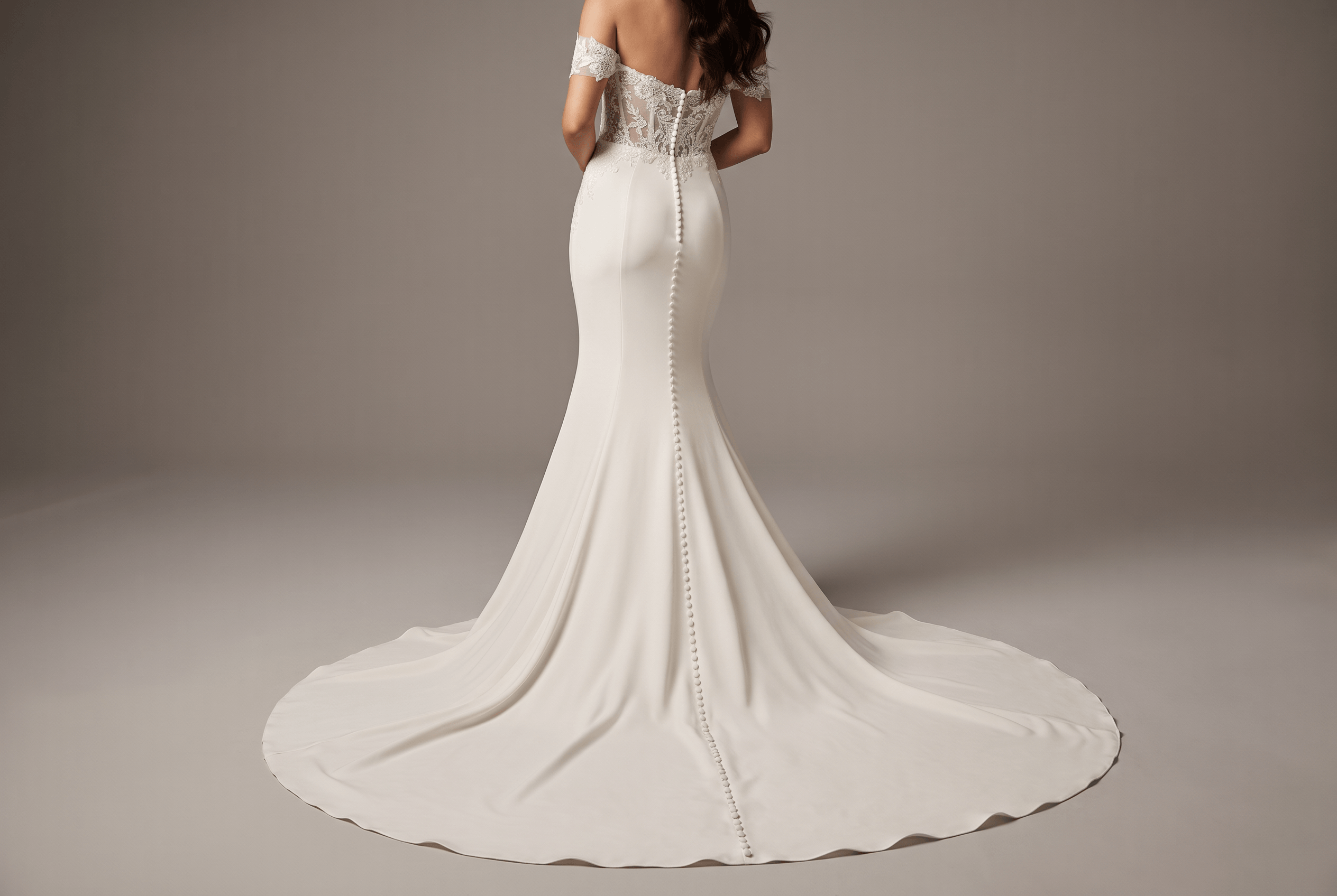 Woman wearing an elegant off-the-shoulder white wedding dress with lace bodice and a long train, shown from the back with a row of buttons running down the center.