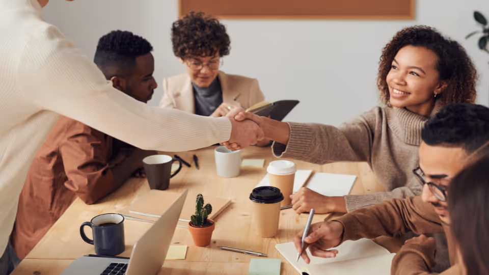 A group of employees working together at a table while two shake hands.