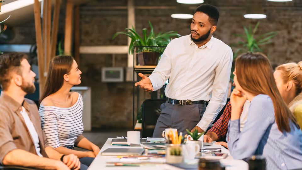 A group of people in an office sitting around a table talking.