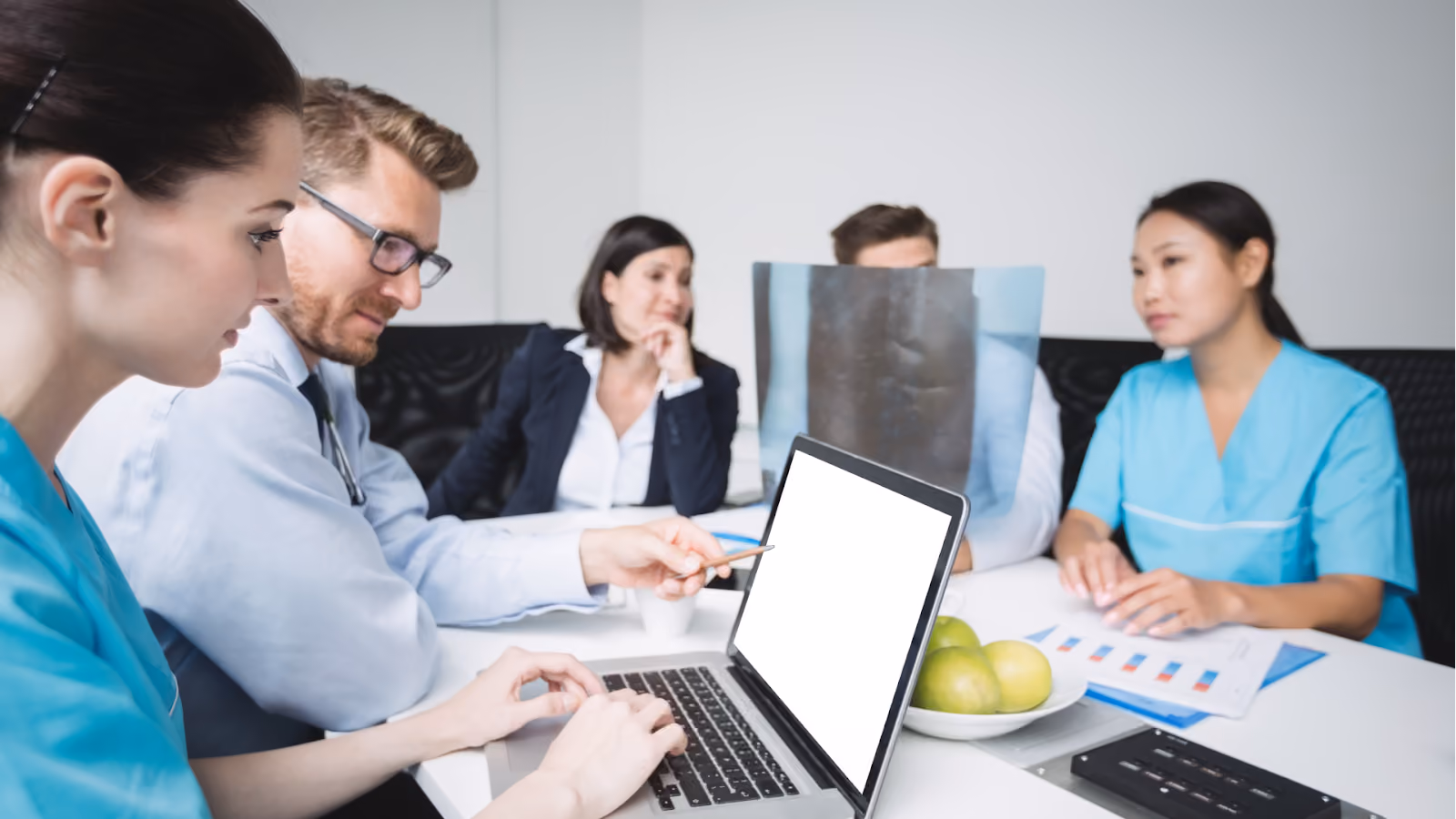 Doctors and nurses in a hospital meeting room discuss reports with laptops on the table.