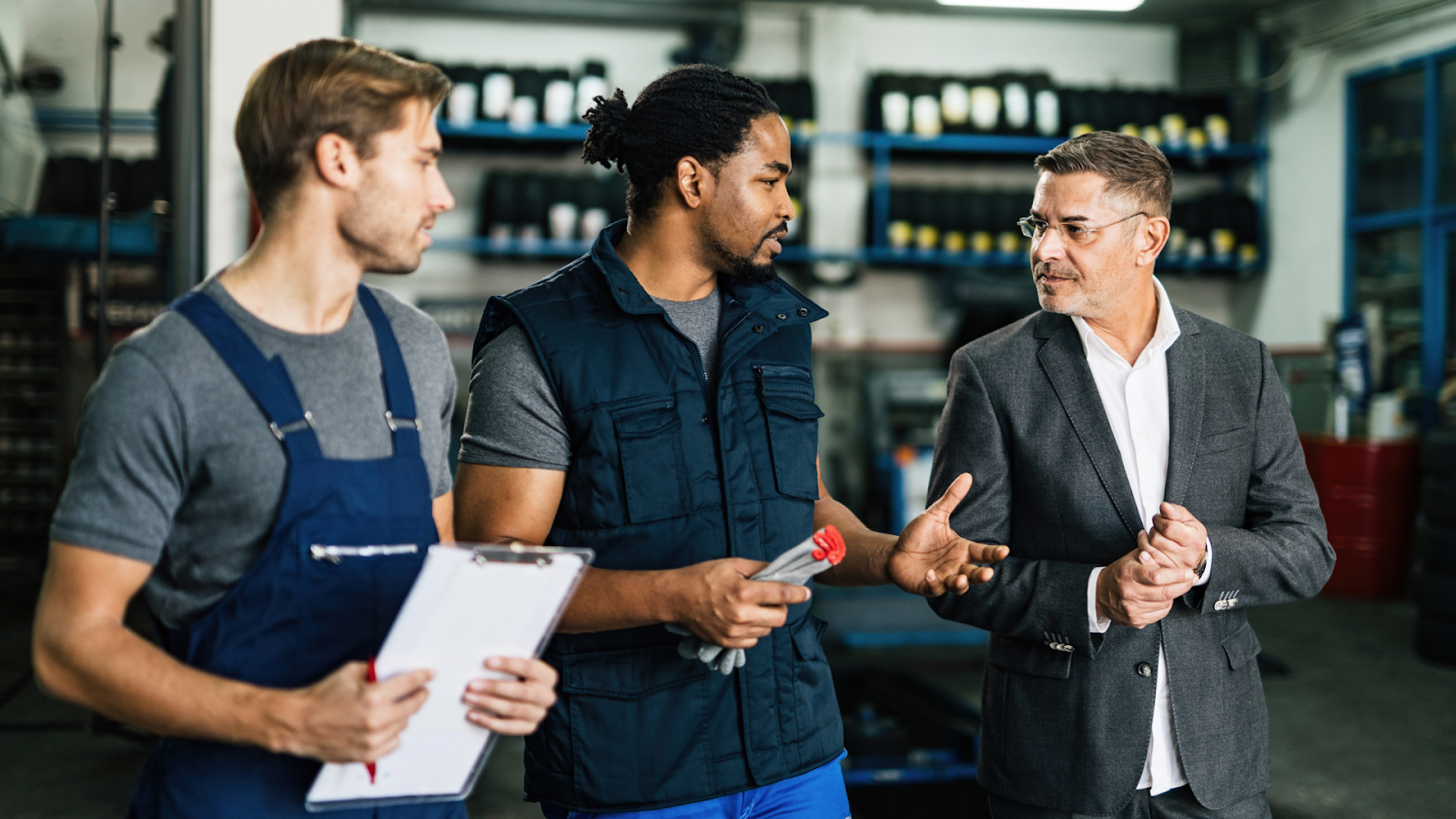 A supervisor engaging in a conversation with two mechanics in an automotive repair shop.
