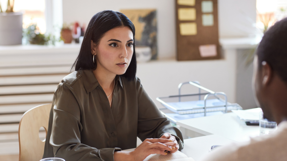  A person sits at a desk looking at another person across from them.