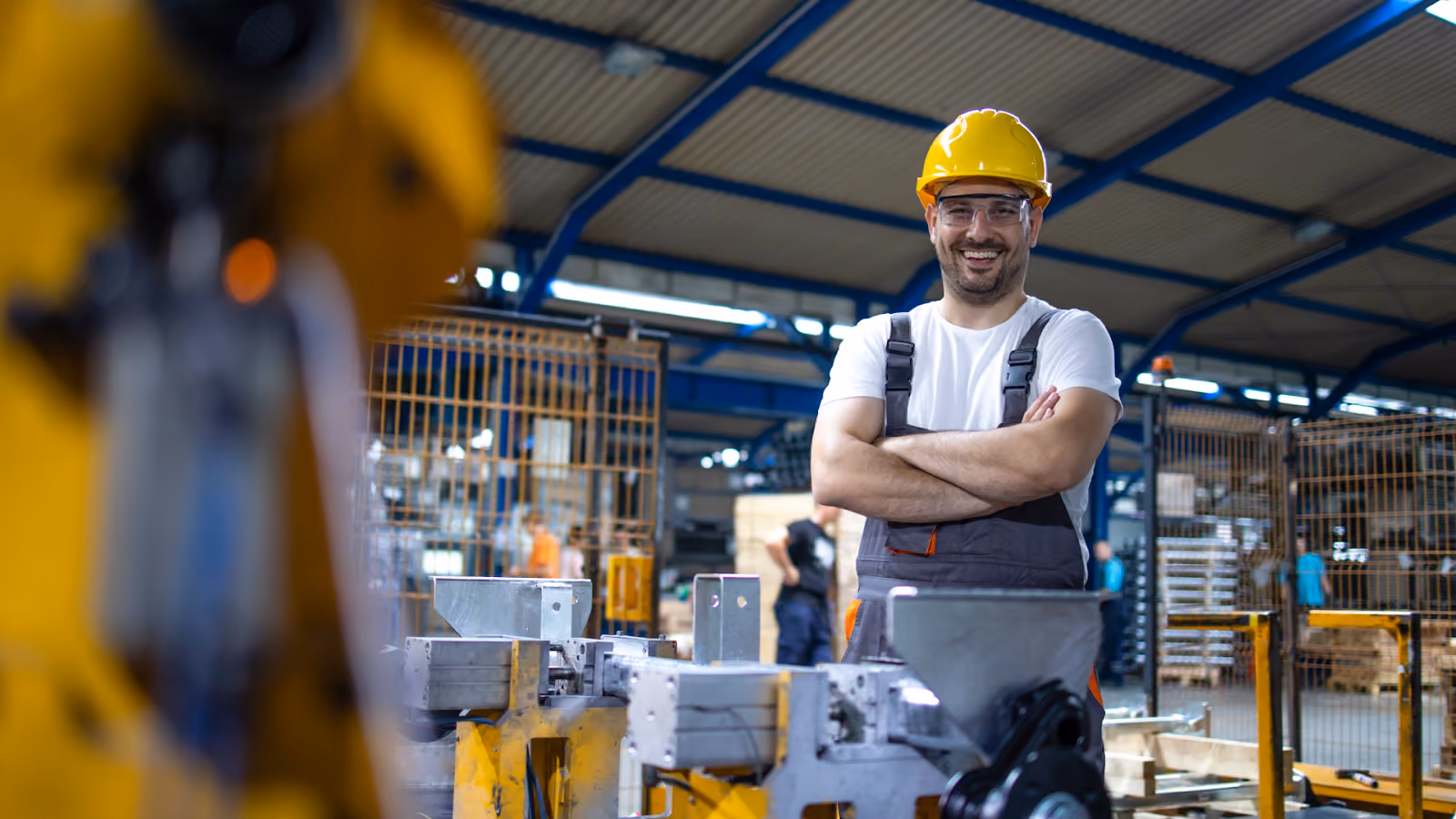 A smiling worker in a yellow hard hat in a warehouse setting.