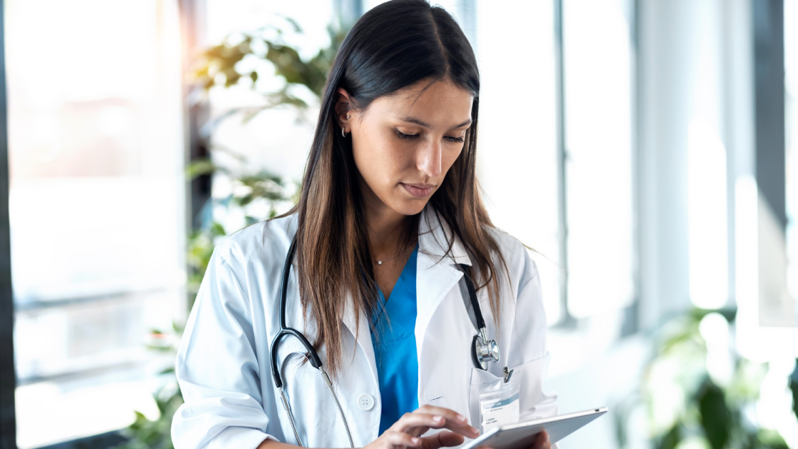 A doctor checks staffing levels and overtime alerts on a tablet during a busy hospital shift to catch overtime risk early.