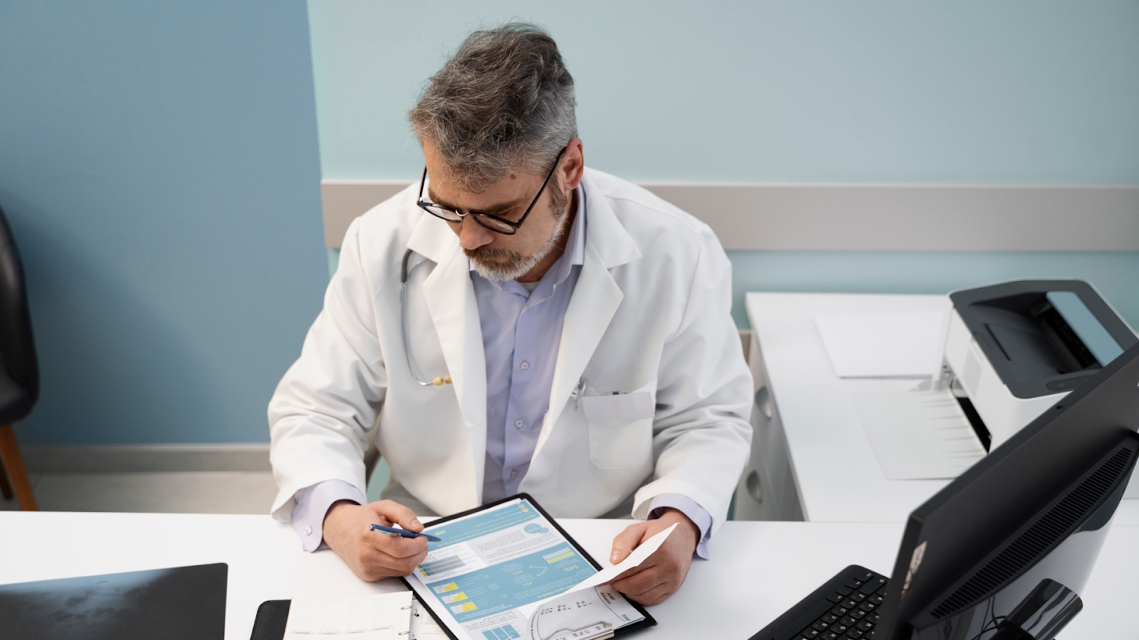 A doctor reviews absence records at a desk as part of staff absence management in a clinical setting.