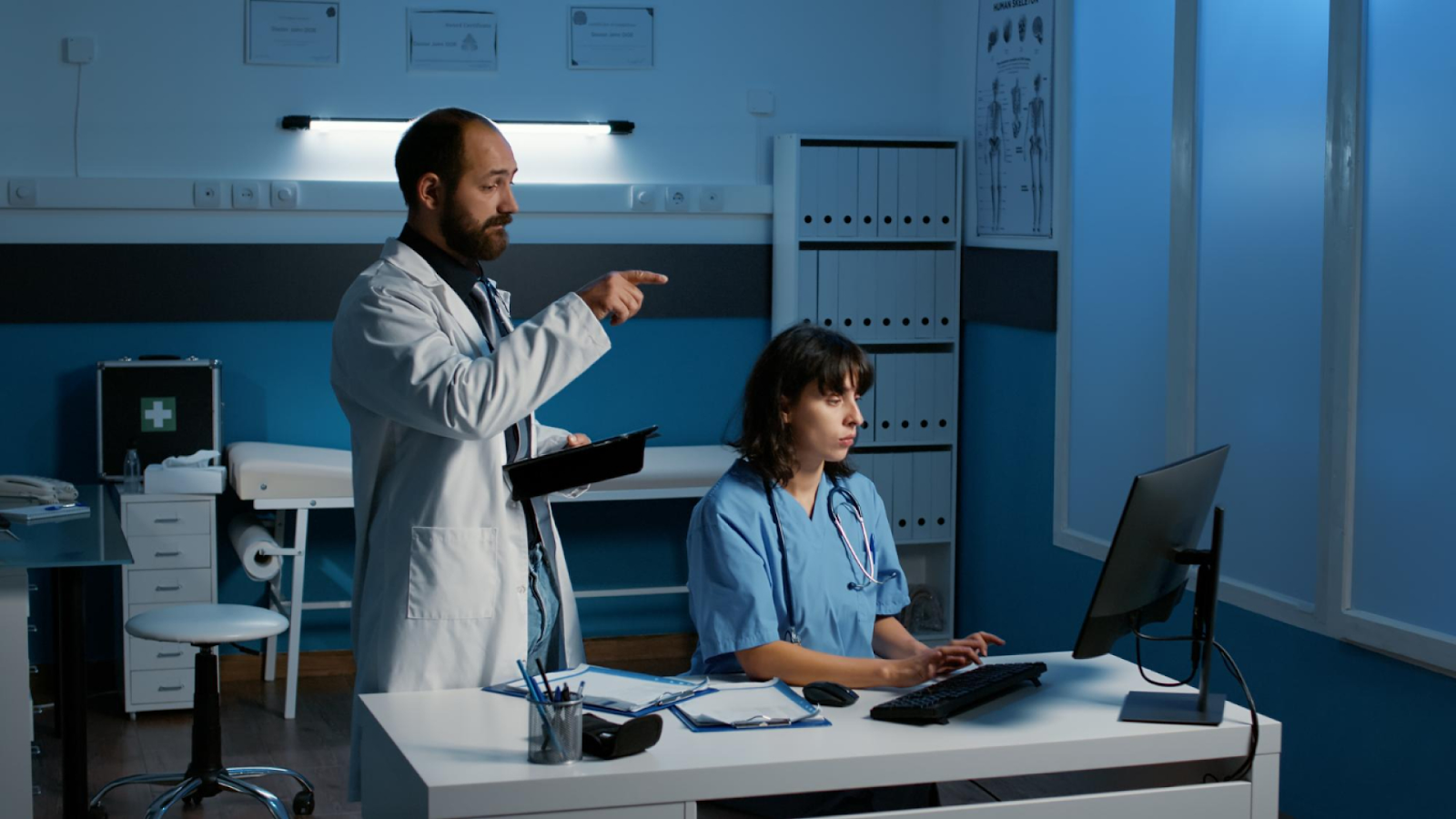 A doctor points toward a computer as a nurse works, highlighting the impact of employee absences on staff.