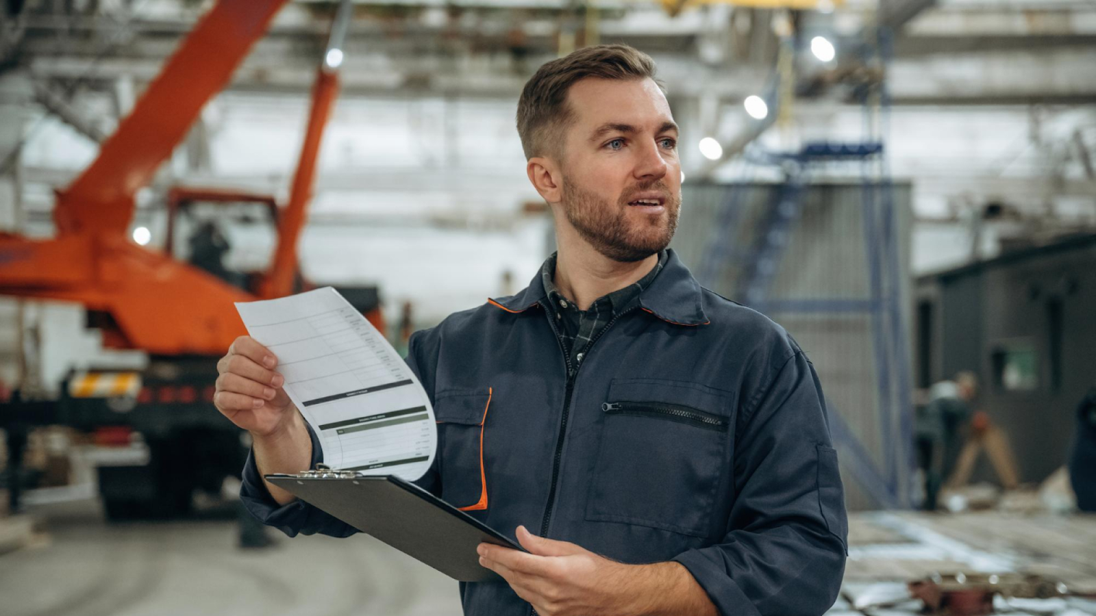 An industrial supervisor reviews coverage plans on a clipboard to manage absences and overtime risk in a manufacturing facility.