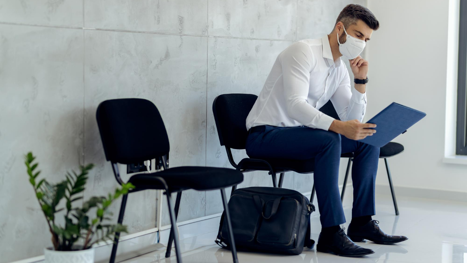 A man wearing a mask sits in a waiting room, illustrating workplace absenteeism and unplanned absences.