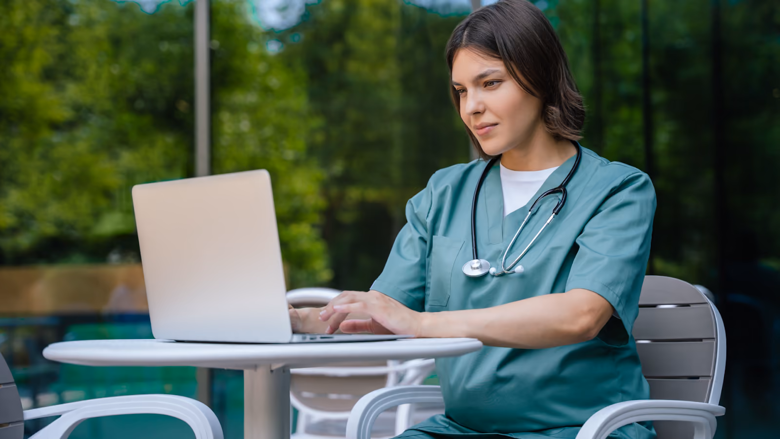  A nurse in green scrubs works on a laptop outdoors, illustrating various 7 shift patterns in healthcare.