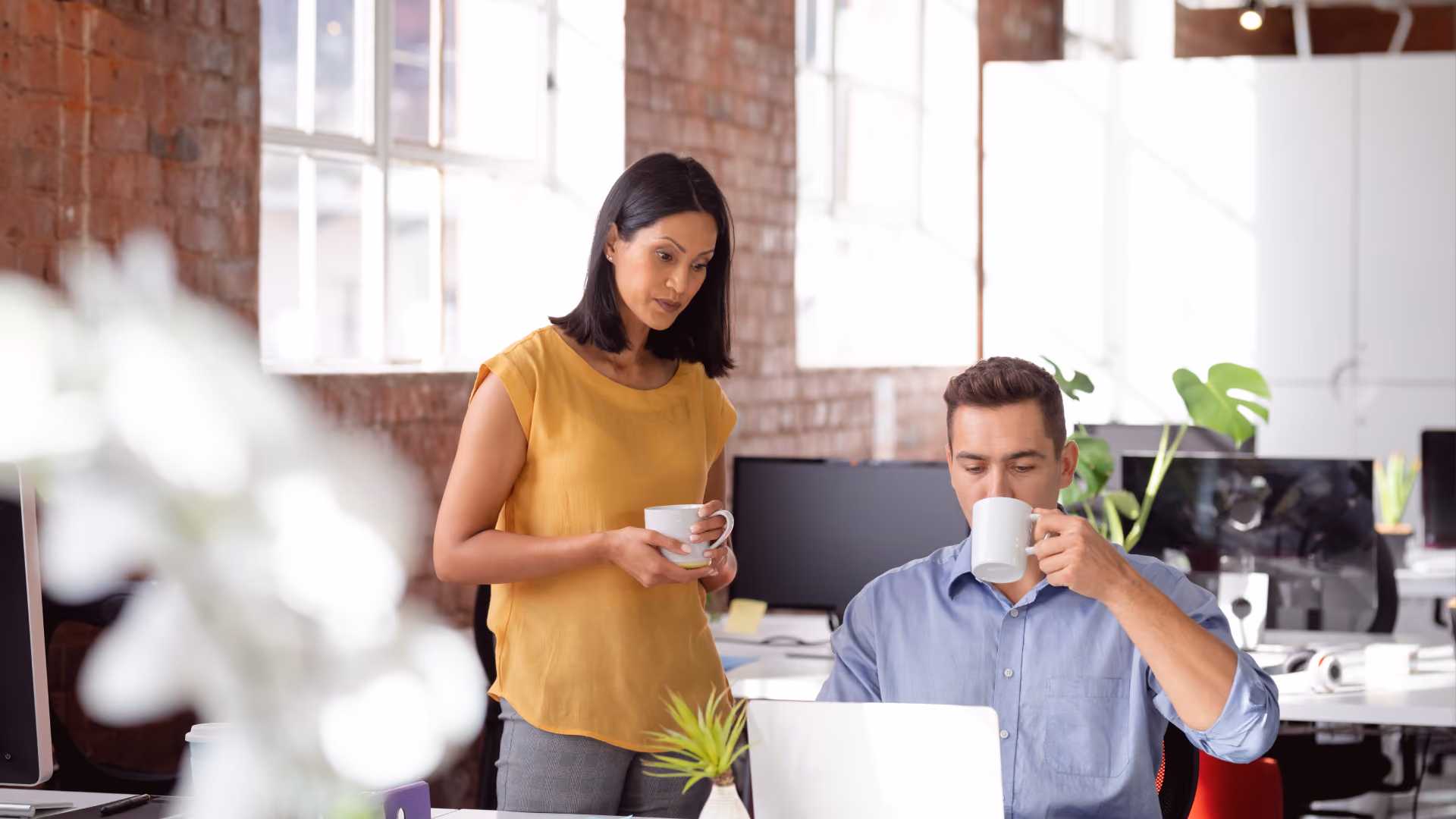 Two colleagues discuss tasks over coffee, addressing how to identify and fix employee scheduling problems.