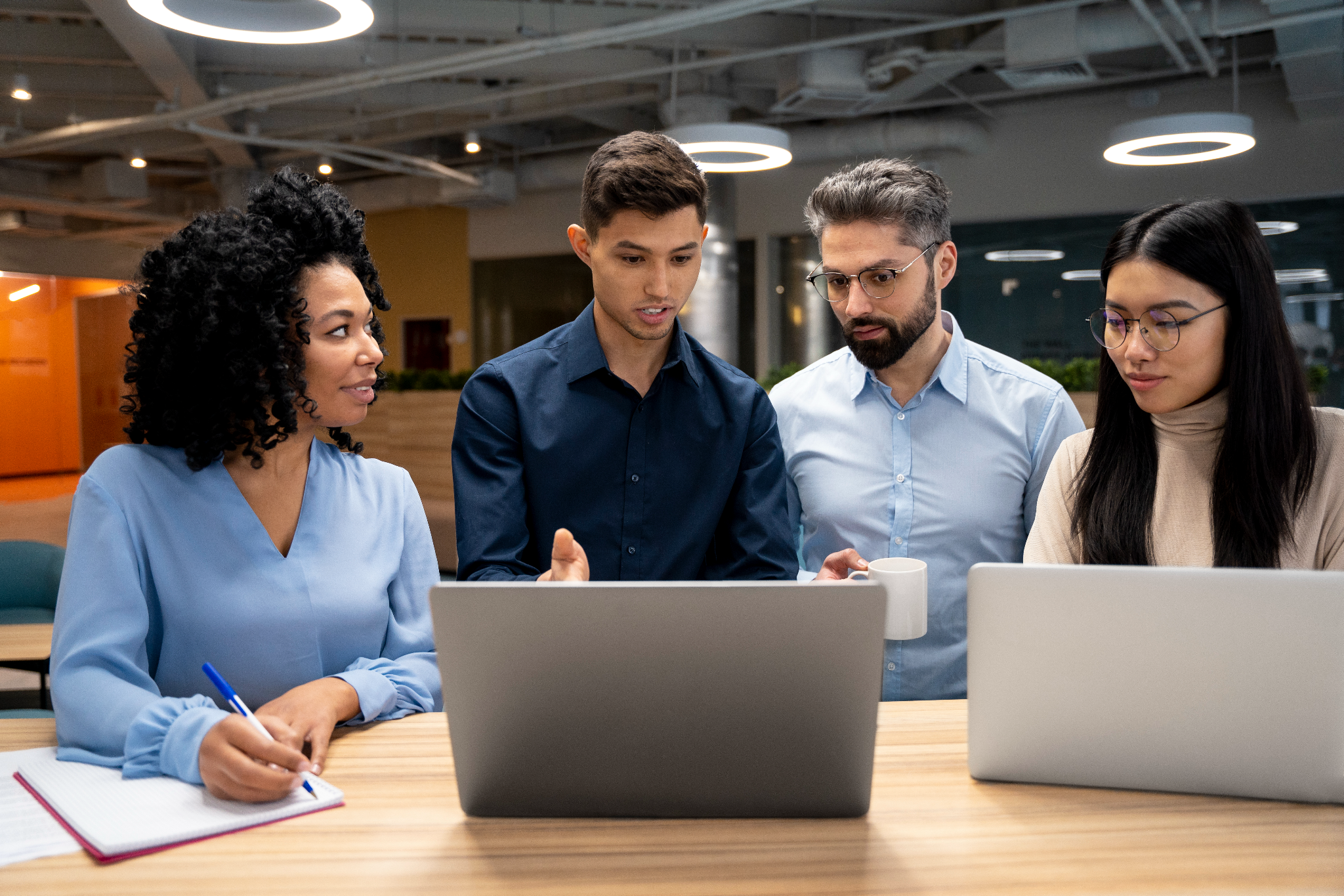A diverse team gathers around laptops, discussing how to mitigate the real cost of scheduling problems.