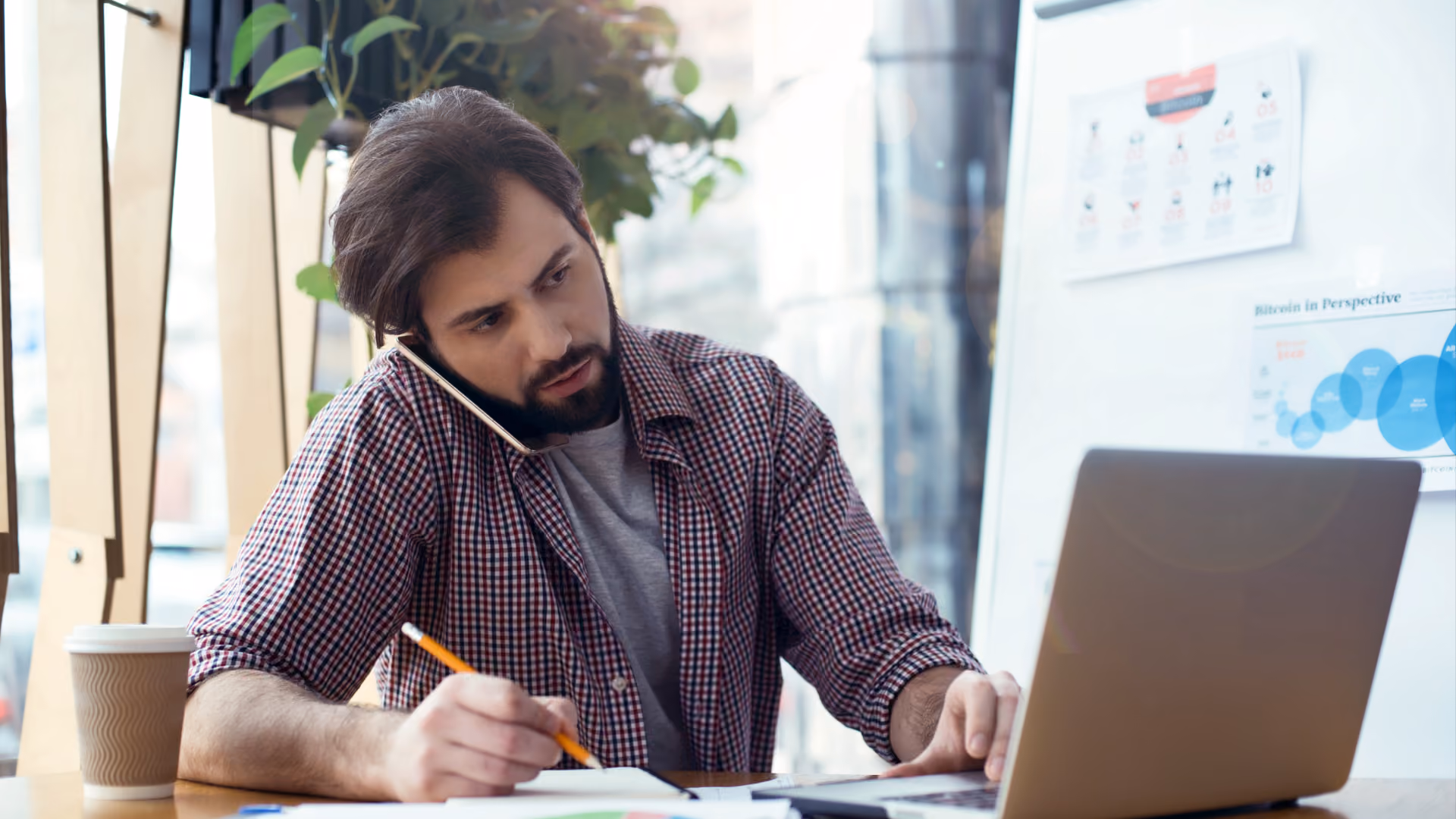 A man works on his laptop and phone, exploring workforce management vs. workforce optimization.