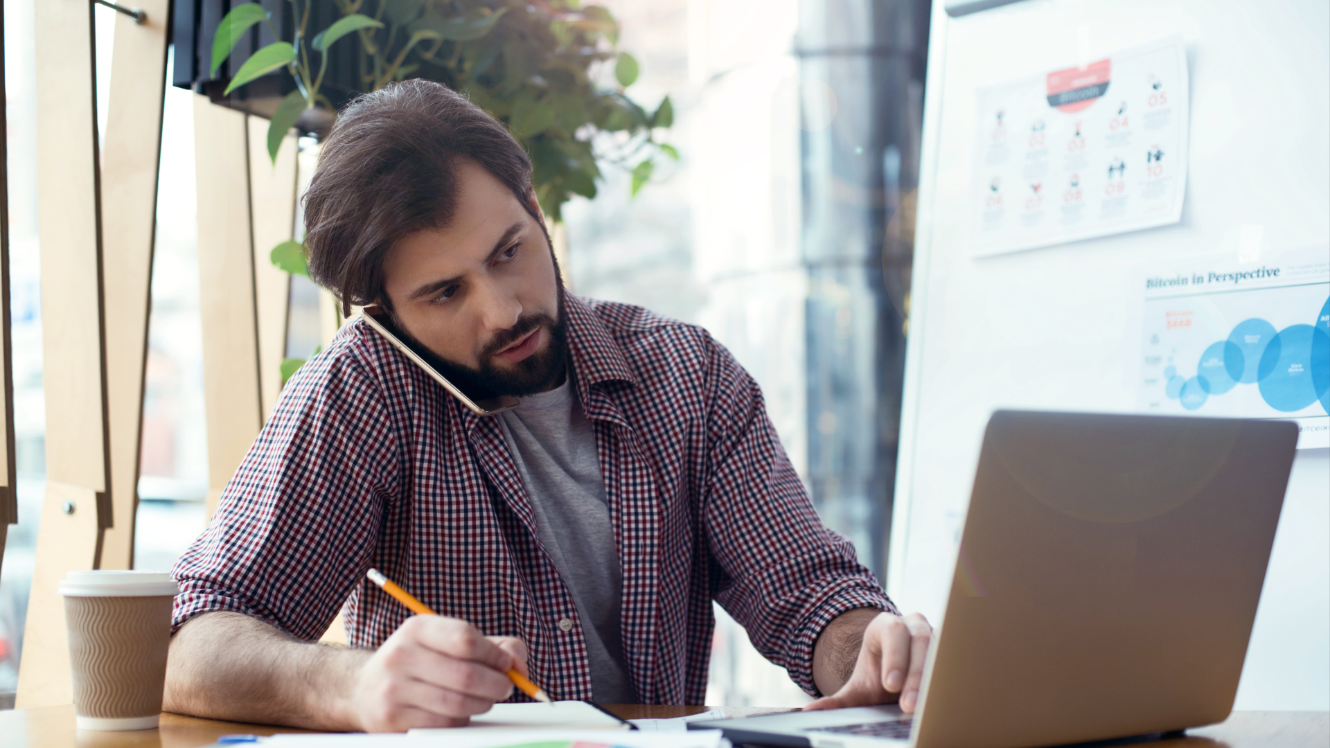 A man works on his laptop and phone, exploring workforce management vs. workforce optimization.