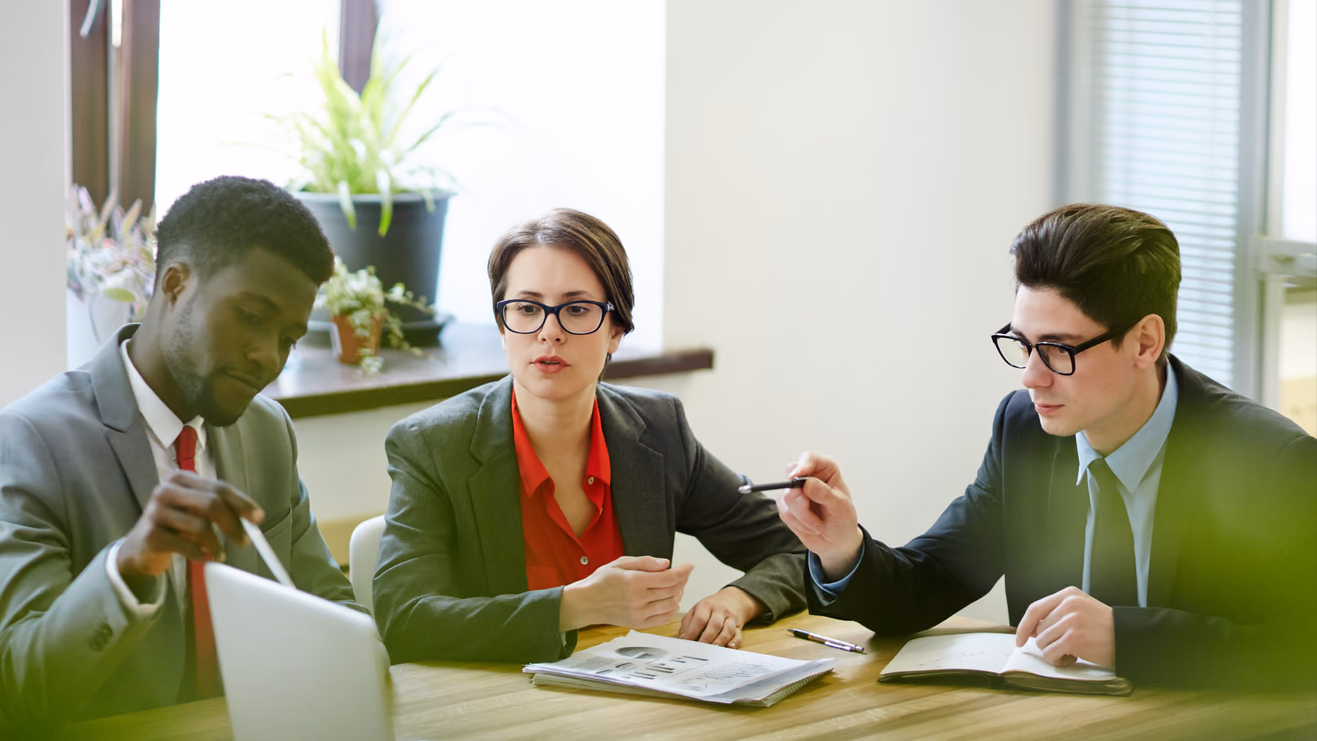Alt text: Three professionals reviewing printed reports and charts together at a conference table.