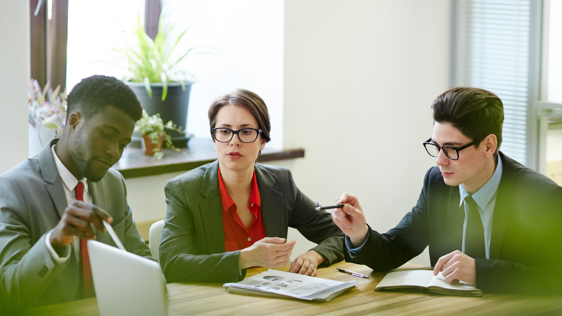 Alt text: Three professionals reviewing printed reports and charts together at a conference table.