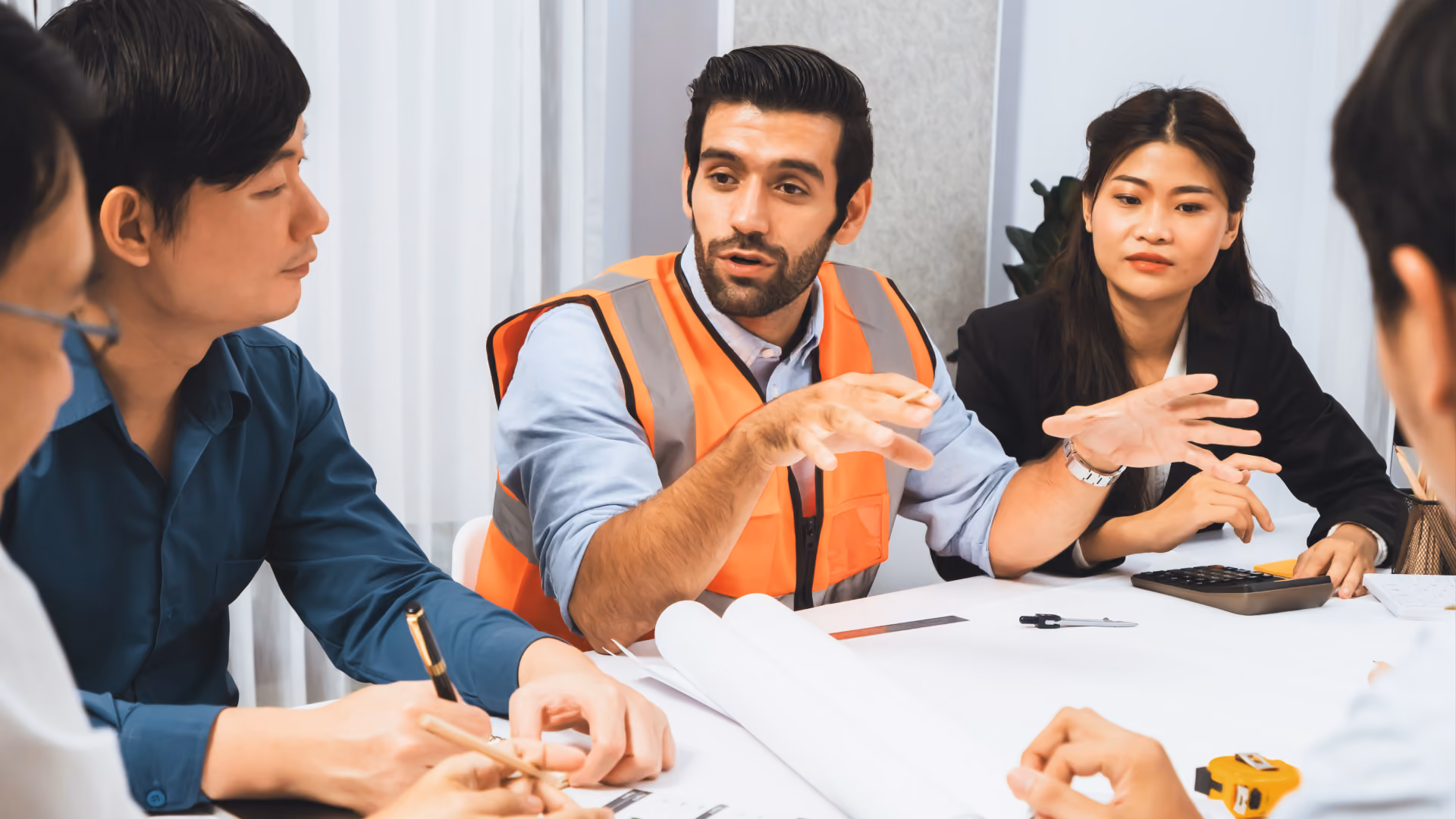 Alt text: Manager in a safety vest leading a cost-planning discussion with colleagues around a table.