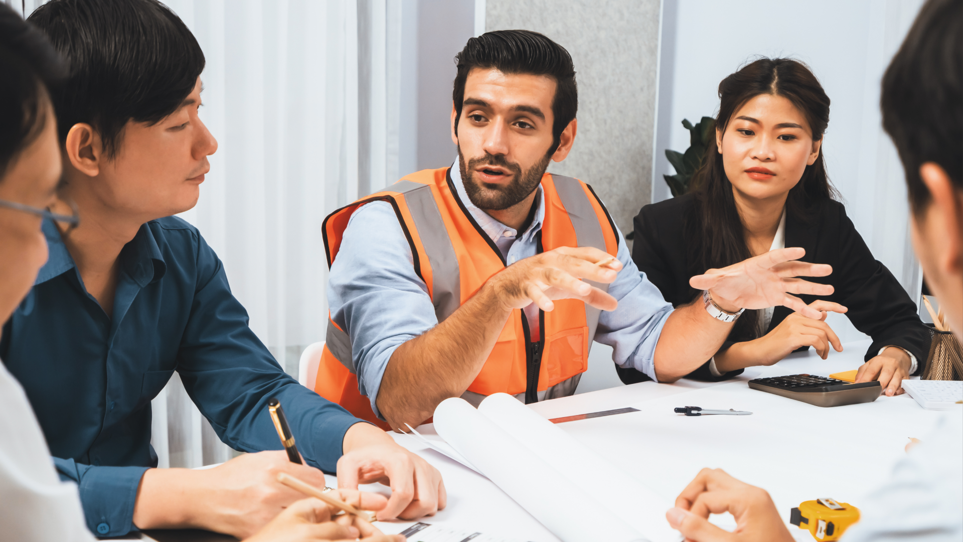 Alt text: Manager in a safety vest leading a cost-planning discussion with colleagues around a table.
