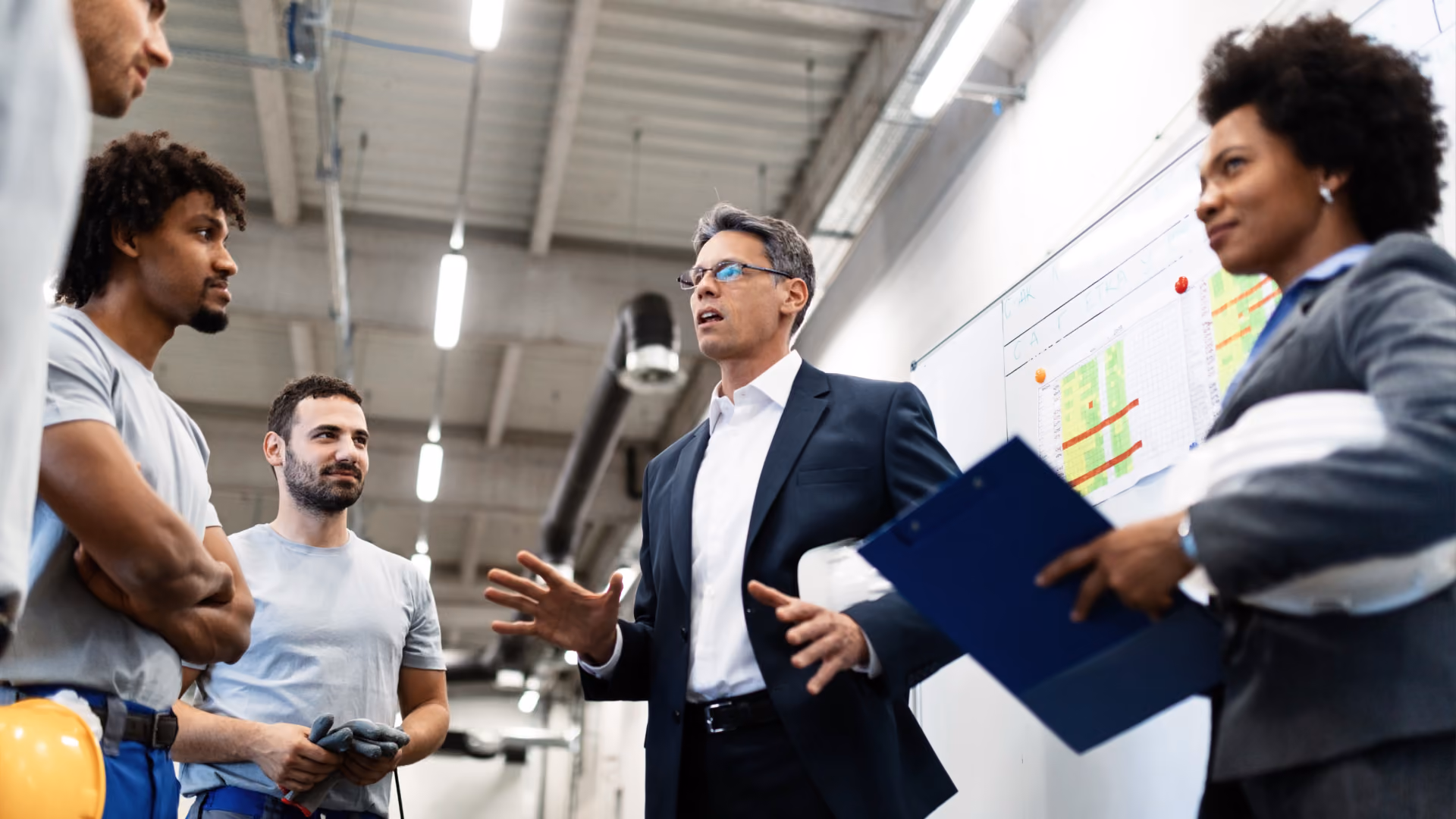 Alt text: Manager discussing a production schedule with workers in front of a planning board.