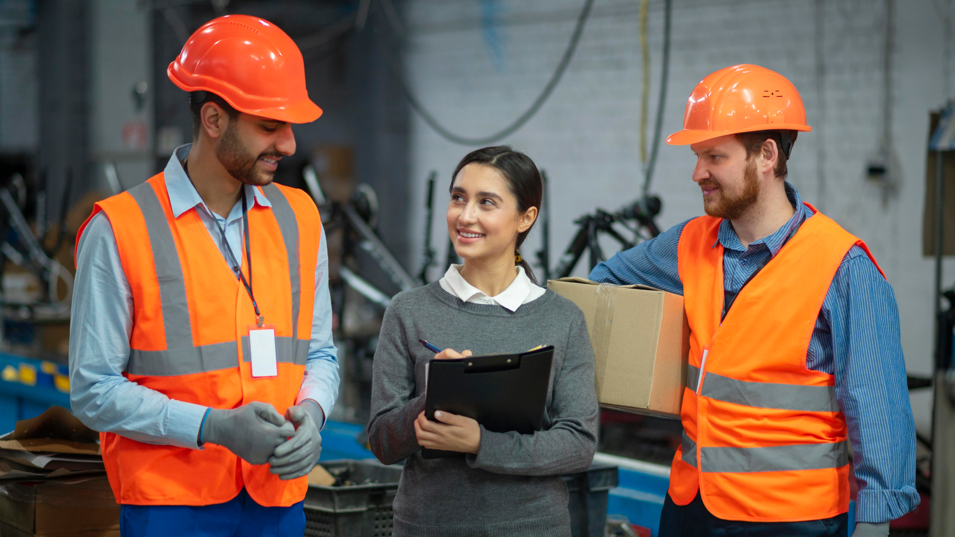 Alt text: Supervisor with a clipboard talking with two warehouse workers on a facility floor.