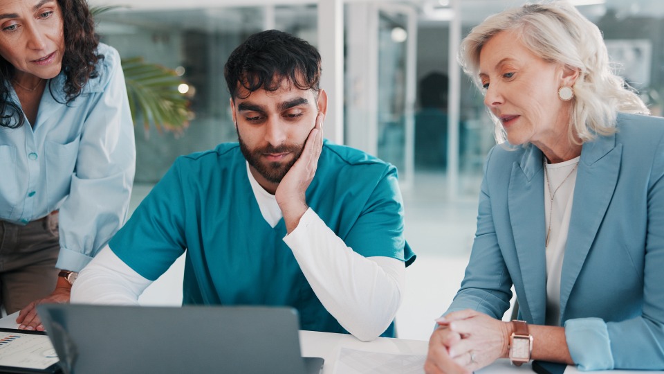 Managers look over a laptop with a healthcare worker, demonstrating how management overrides can undermine administrative systems.