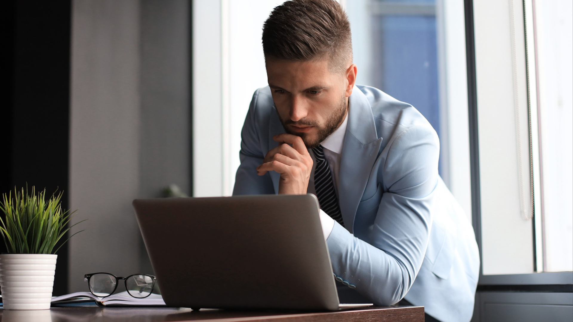 Man leaning over a laptop with his hand on his chin, researching fingerprint time clocks.